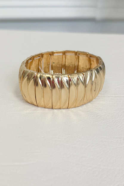 Gold-tone textured bracelet featuring a repeating detailed pattern across the band on a white studio background