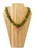 A beaded necklace with olive green faceted beads and a small carved pink heart pendant, displayed on a light wood stand against a white background.