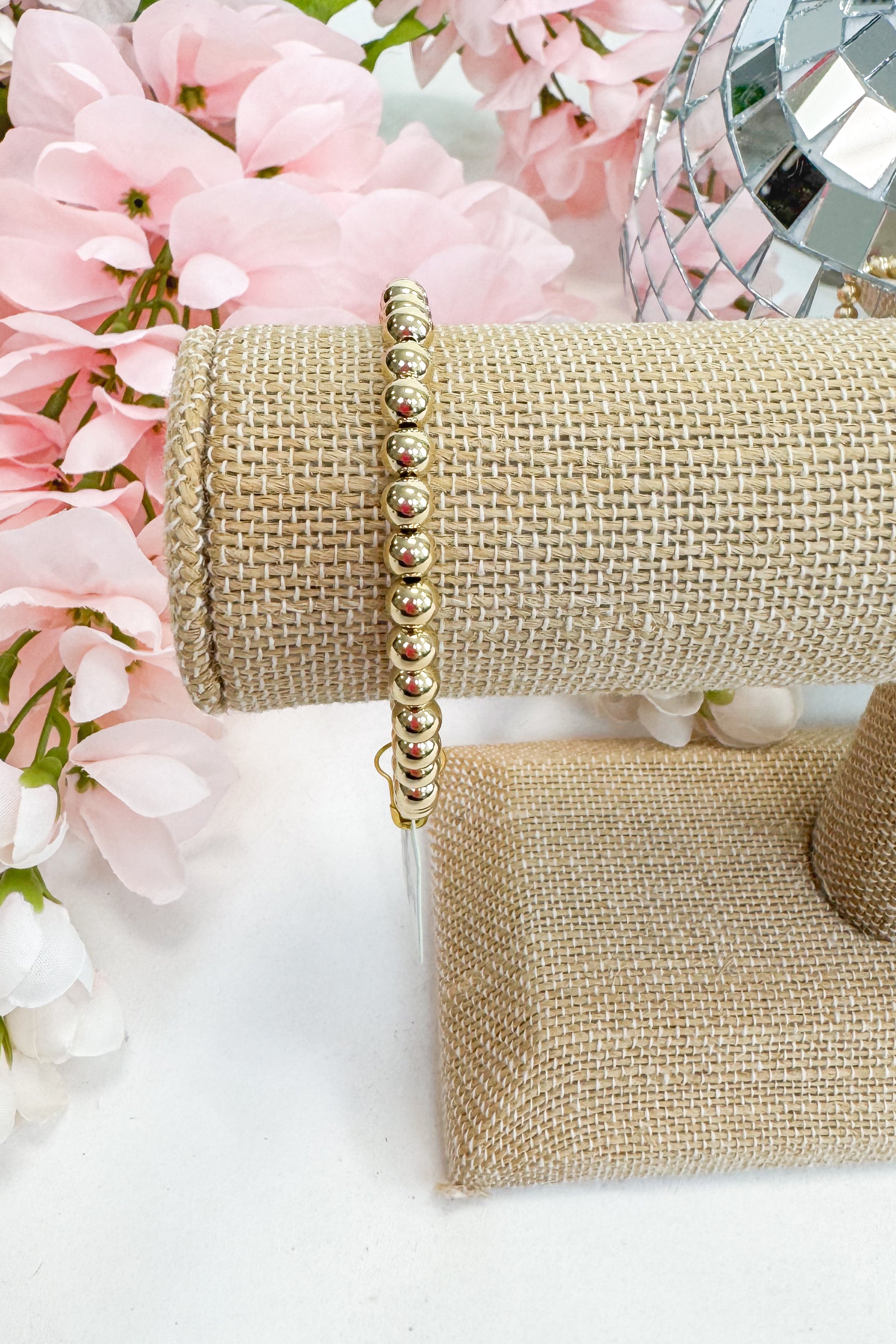 gold enewton bracelet on burlap display with floral background