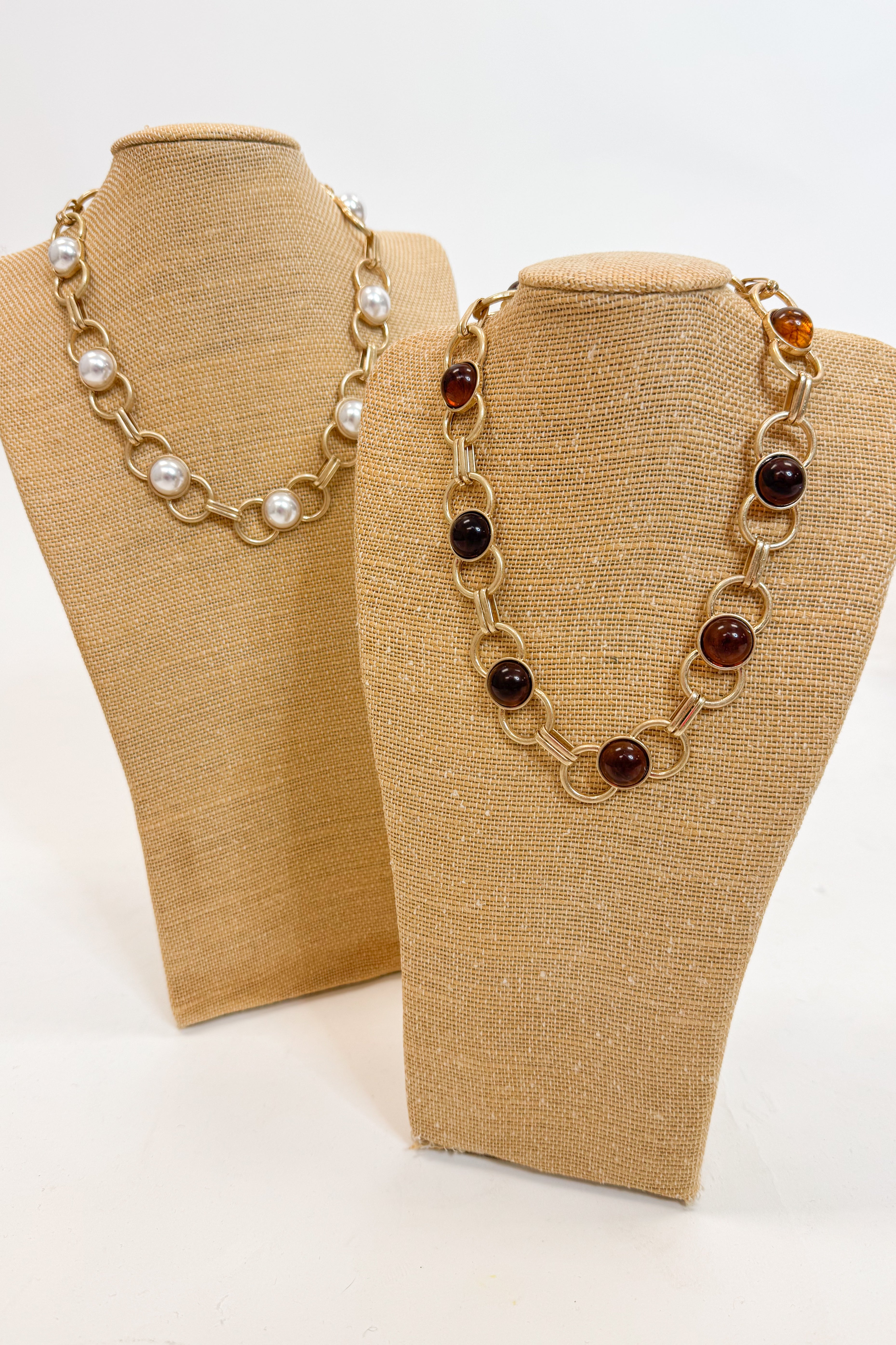 Two necklaces on mannequin busts with a plain background