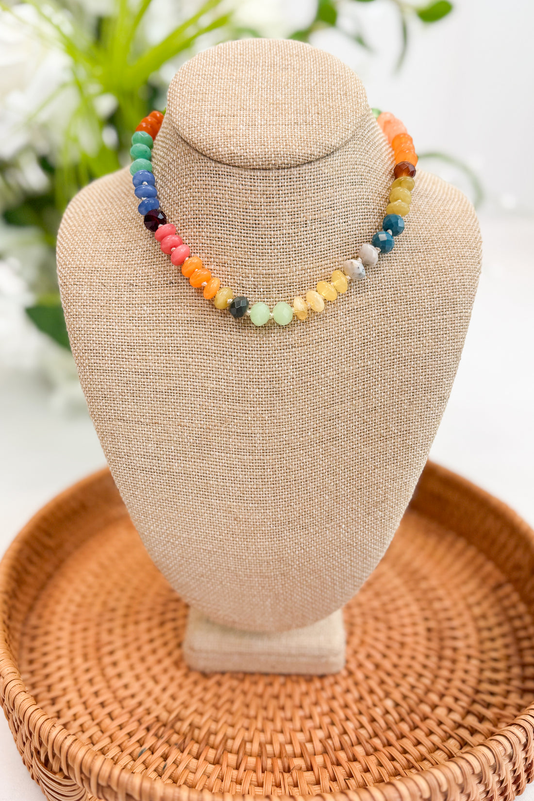 Colorful beaded necklace on a beige bust with a blurred floral background