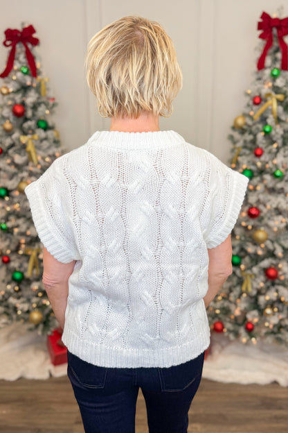 Person wearing a white cable knit sweater in front of Christmas trees.