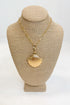 Gold necklace with a shell pendant on a beige mannequin bust against a white background