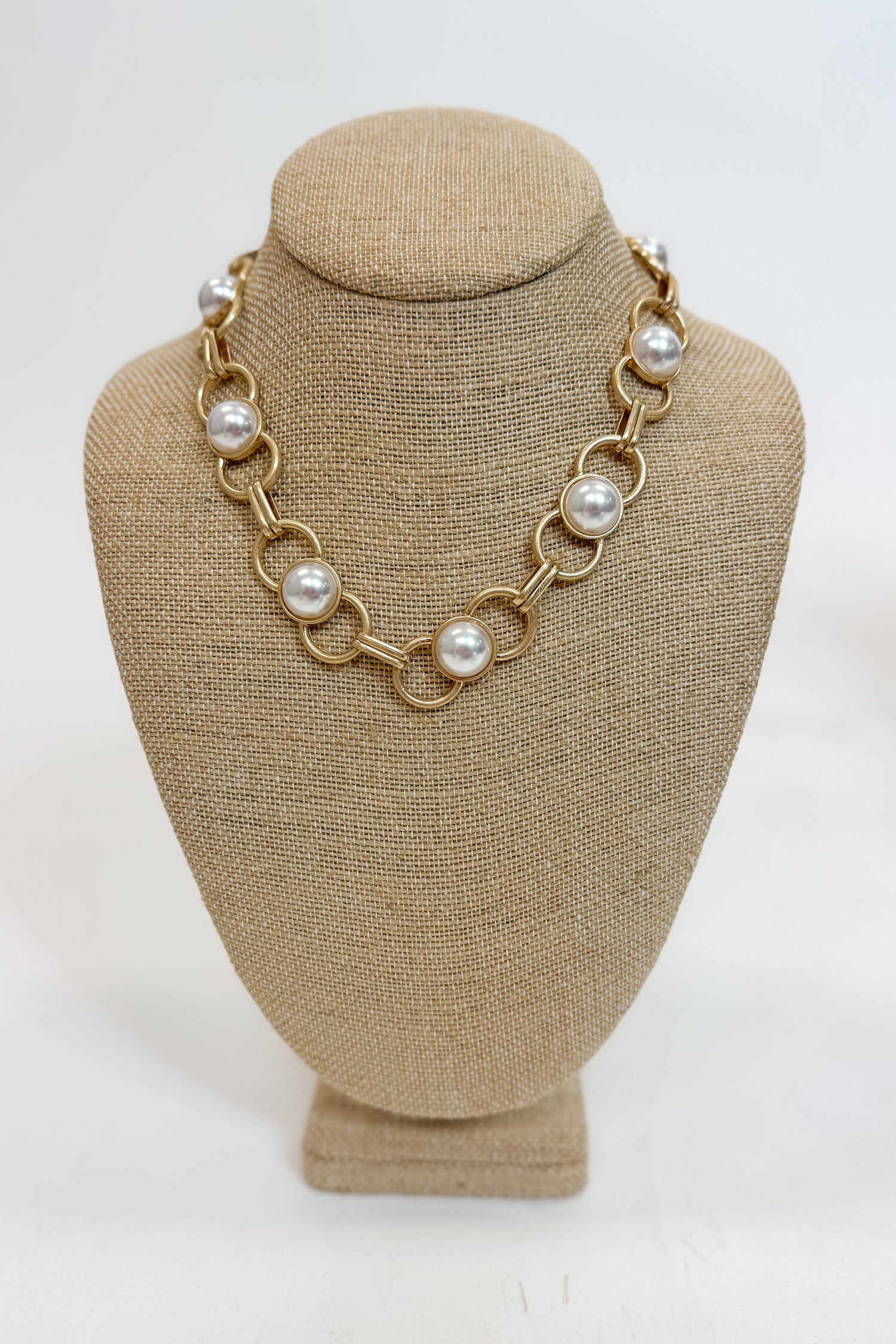 Gold chain necklace with pearls on a beige mannequin bust against a white background