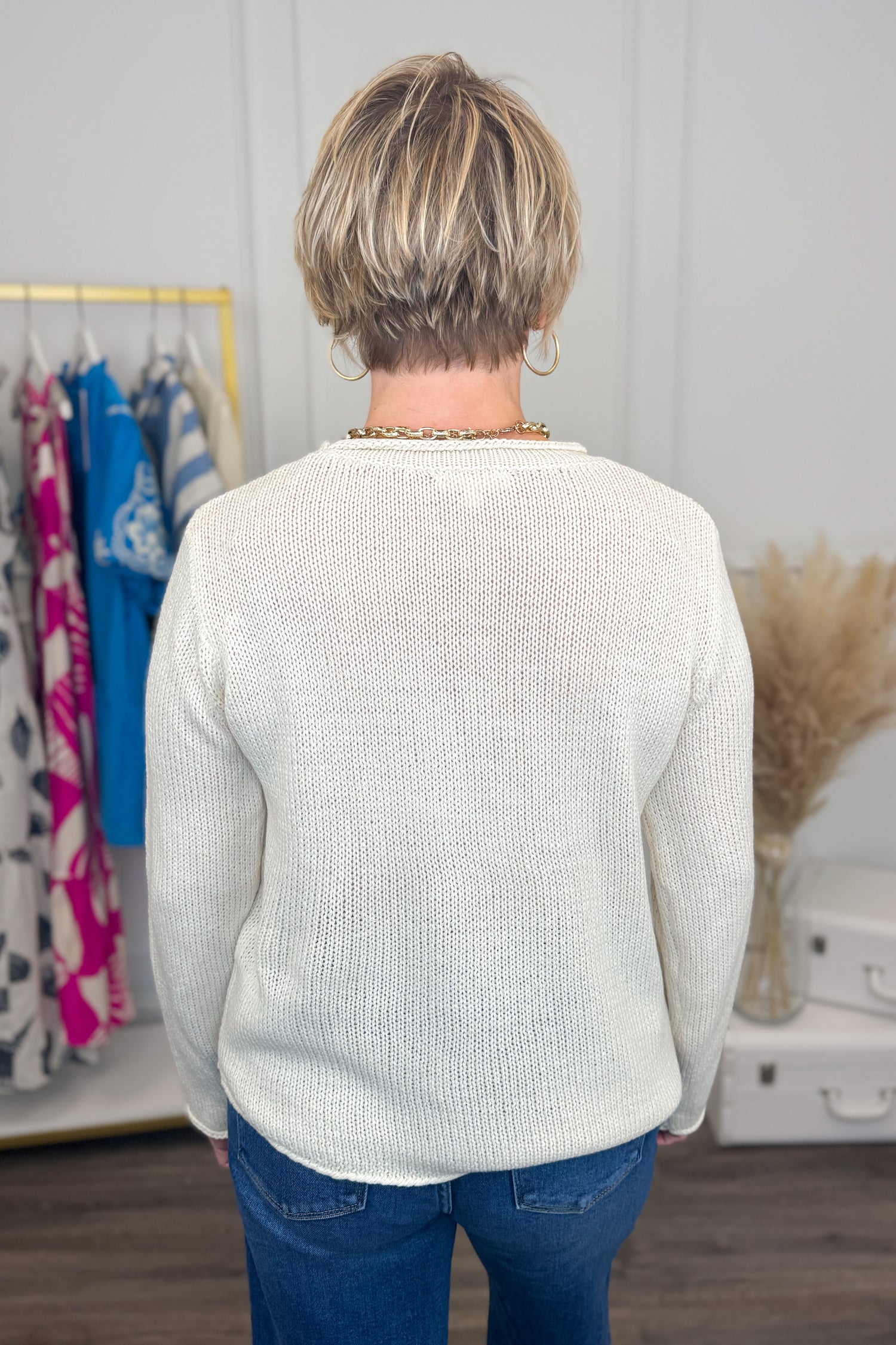 Person wearing a white sweater in a room with clothes and decor.