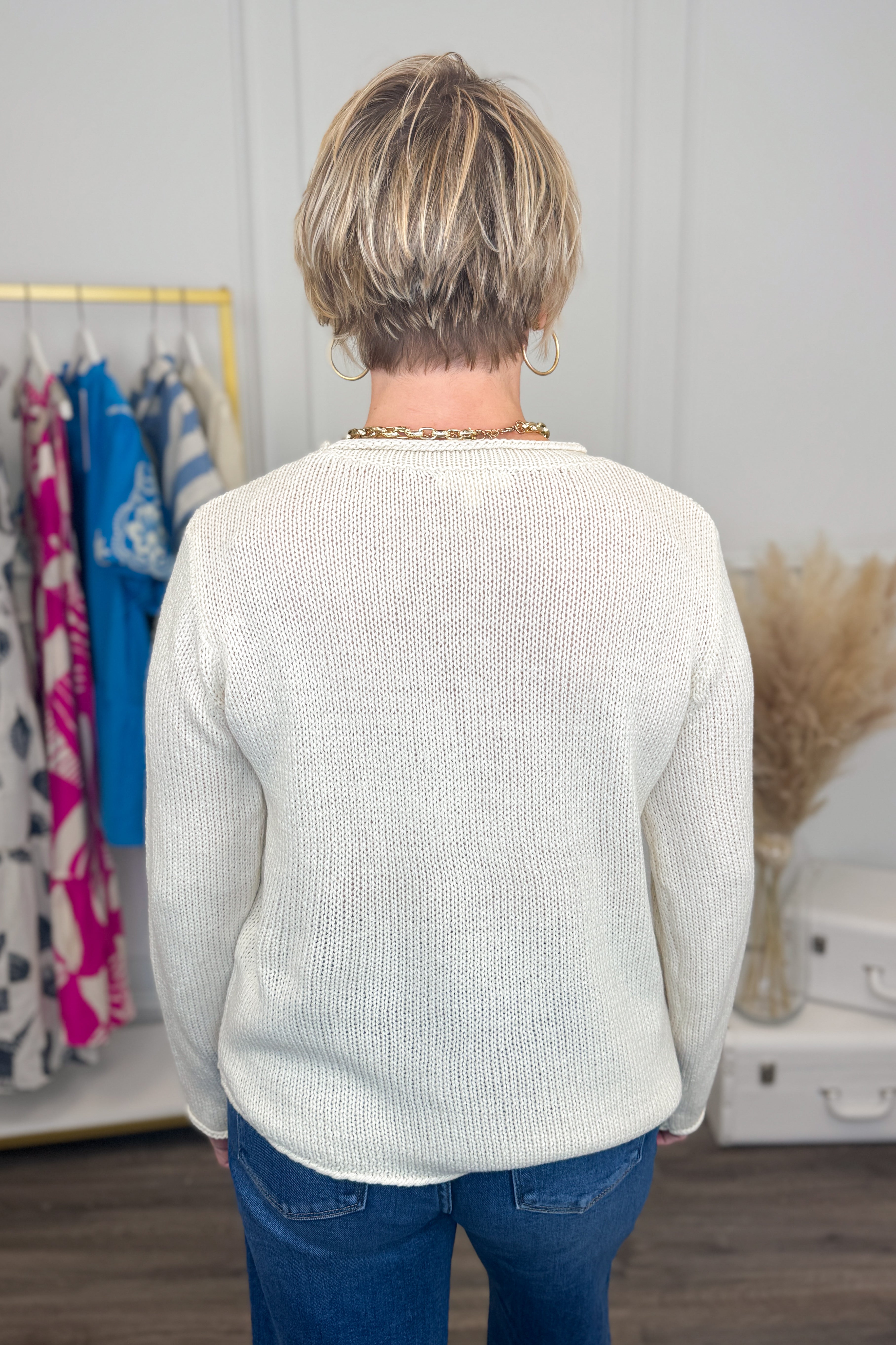 Person wearing a white sweater in a room with clothes and decor.