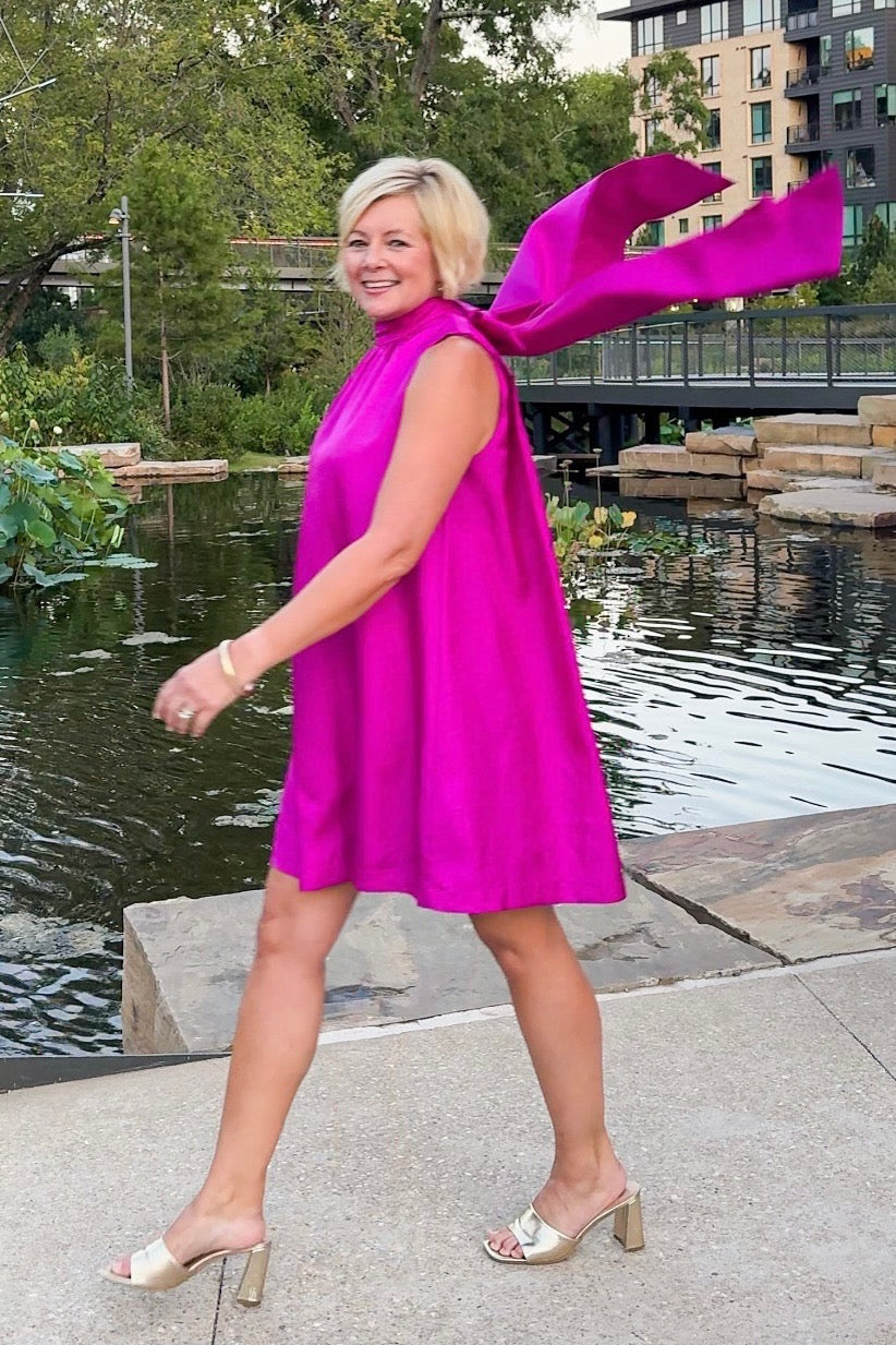 Woman in a bright pink dress with a large bow standing by a pond.