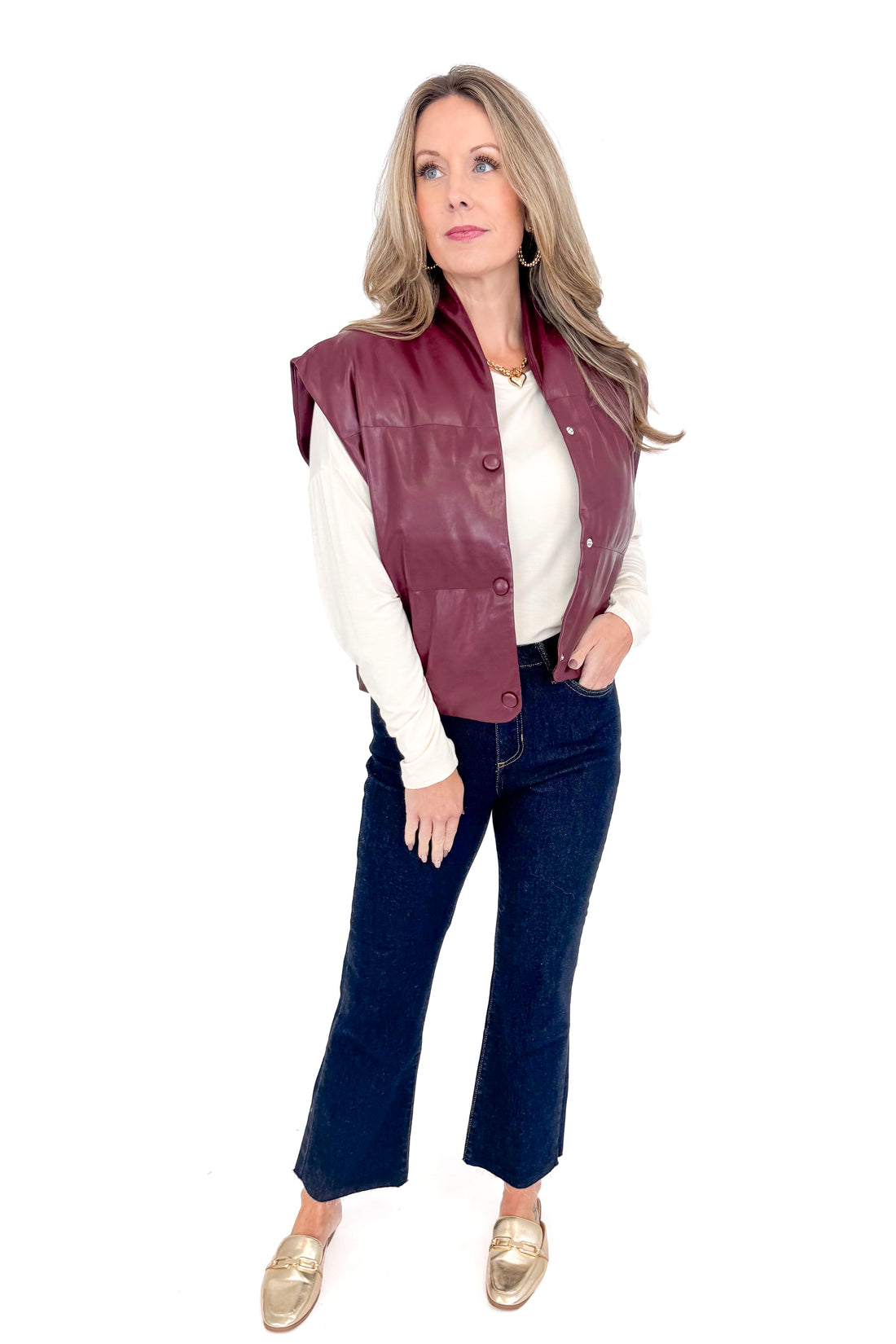 Front view of woman wearing plum faux leather vest with jeans against white studio background.