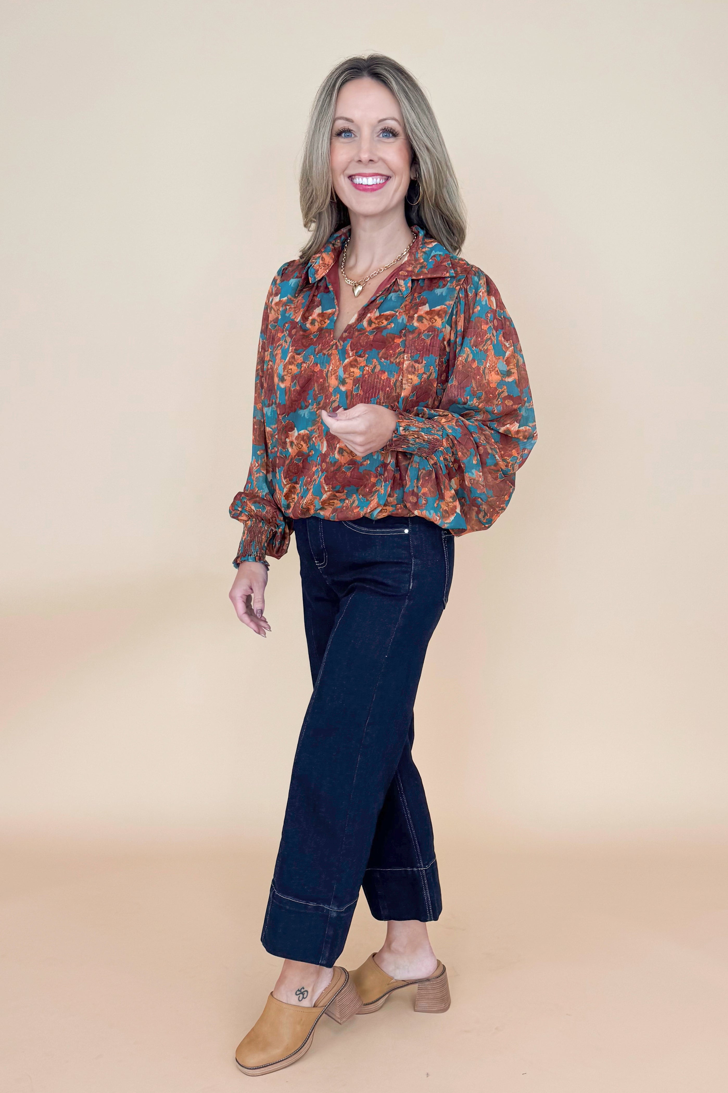 Side view of woman wearing Brown &amp; Teal Printed Top and jeans in a studio with tan background.