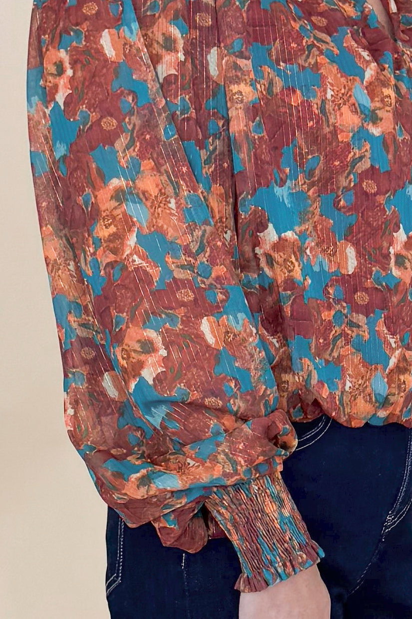 Detailed view of Woman wearing Brown &amp; Teal Printed Top and jeans in a studio with tan background.