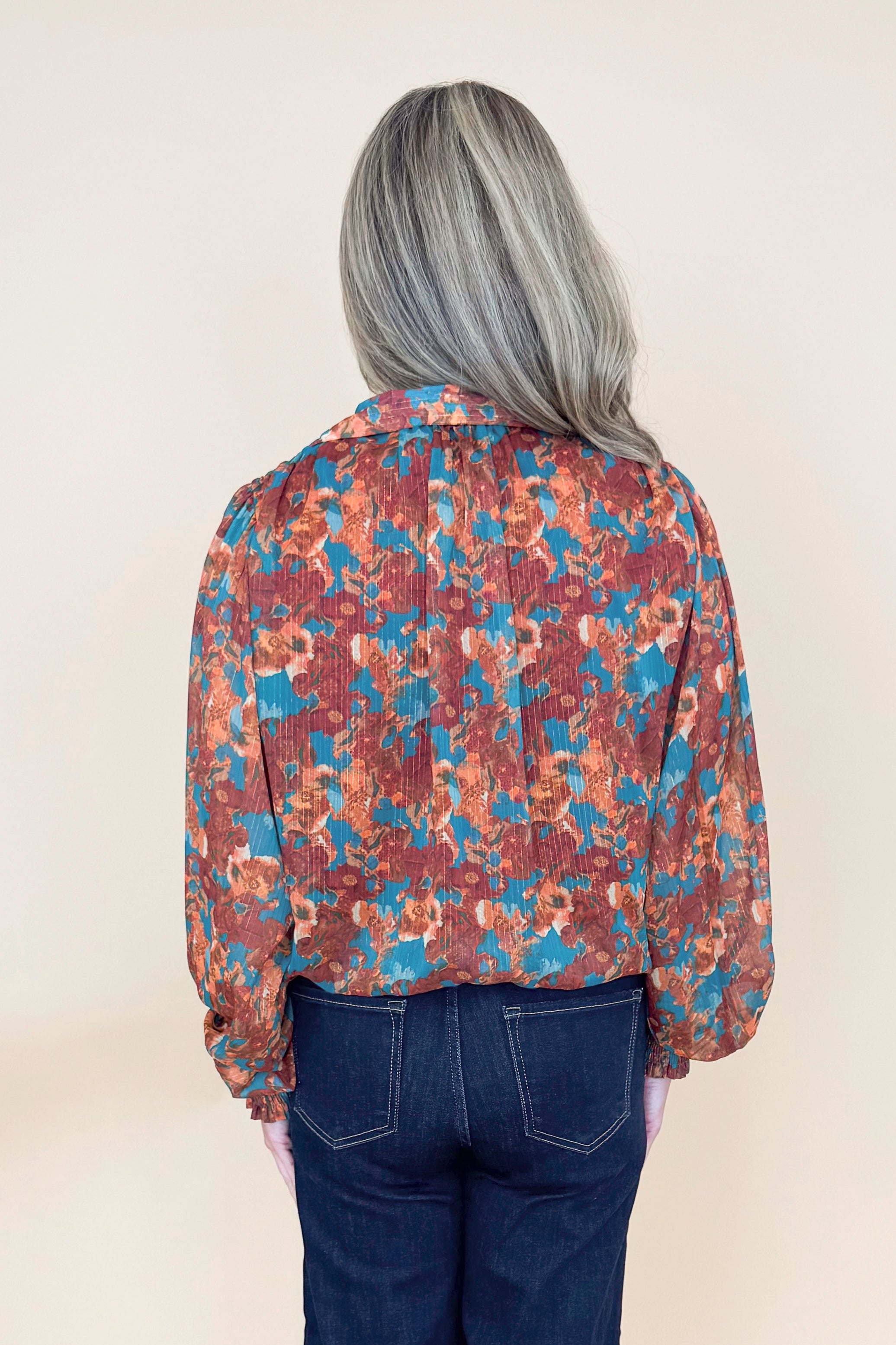Back view of woman wearing Brown &amp; Teal Printed Top and jeans in a studio with tan background.