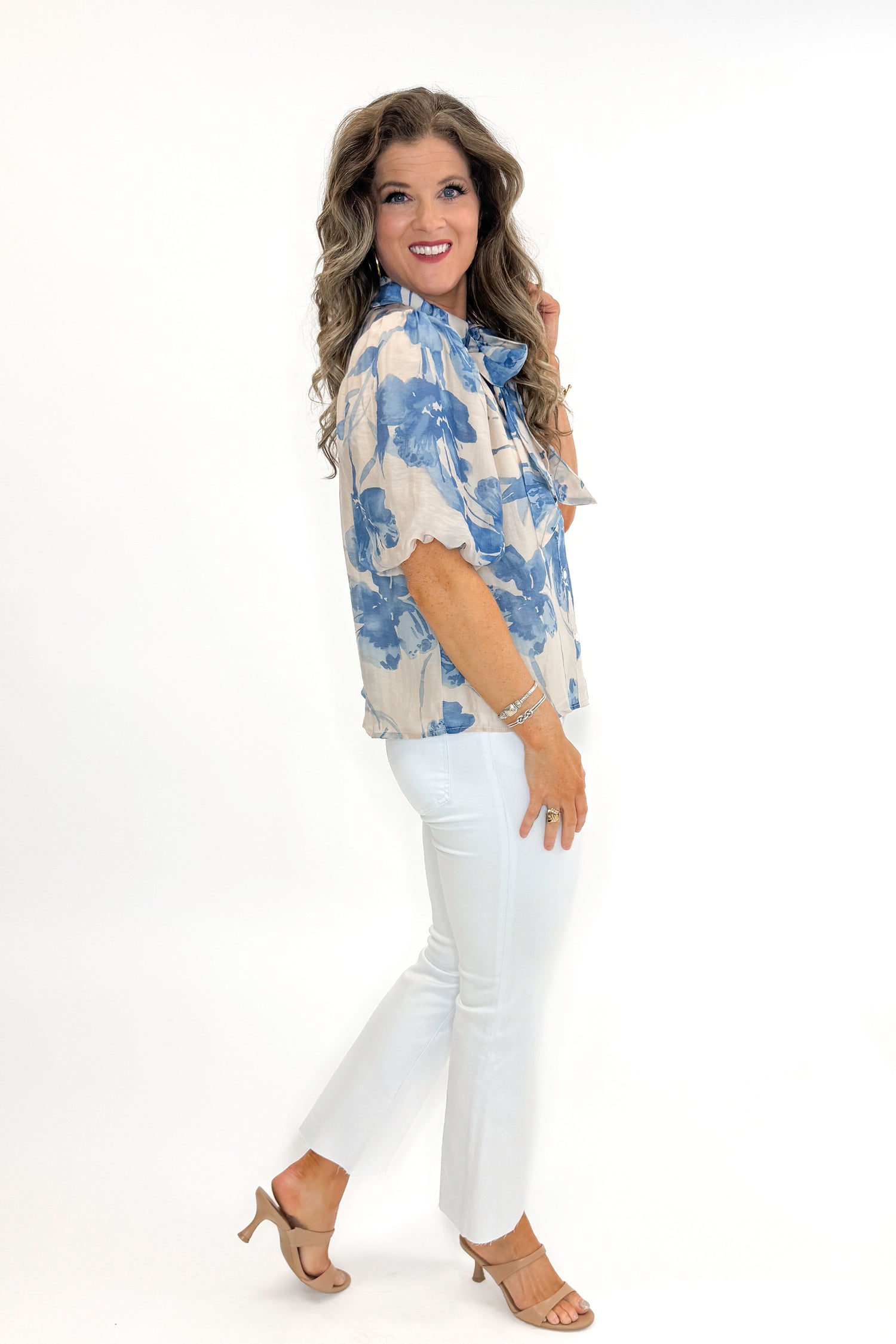 Side view of woman wearing Cream &amp; Blue Floral Neck Tie Detail Top by Fate with white jeans against white studio background.