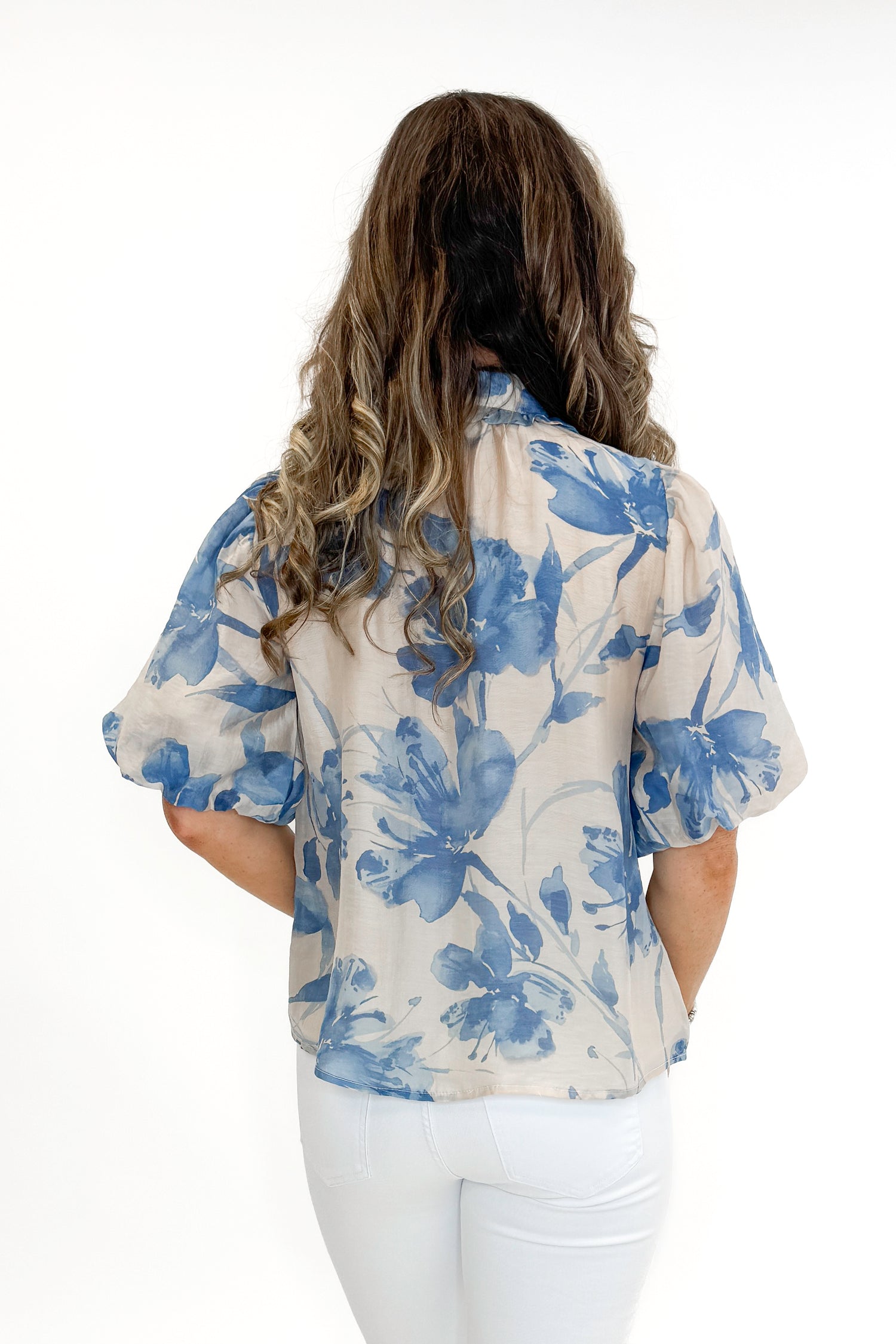 Back view of woman wearing Cream &amp; Blue Floral Neck Tie Detail Top by Fate with white jeans against white studio background.
