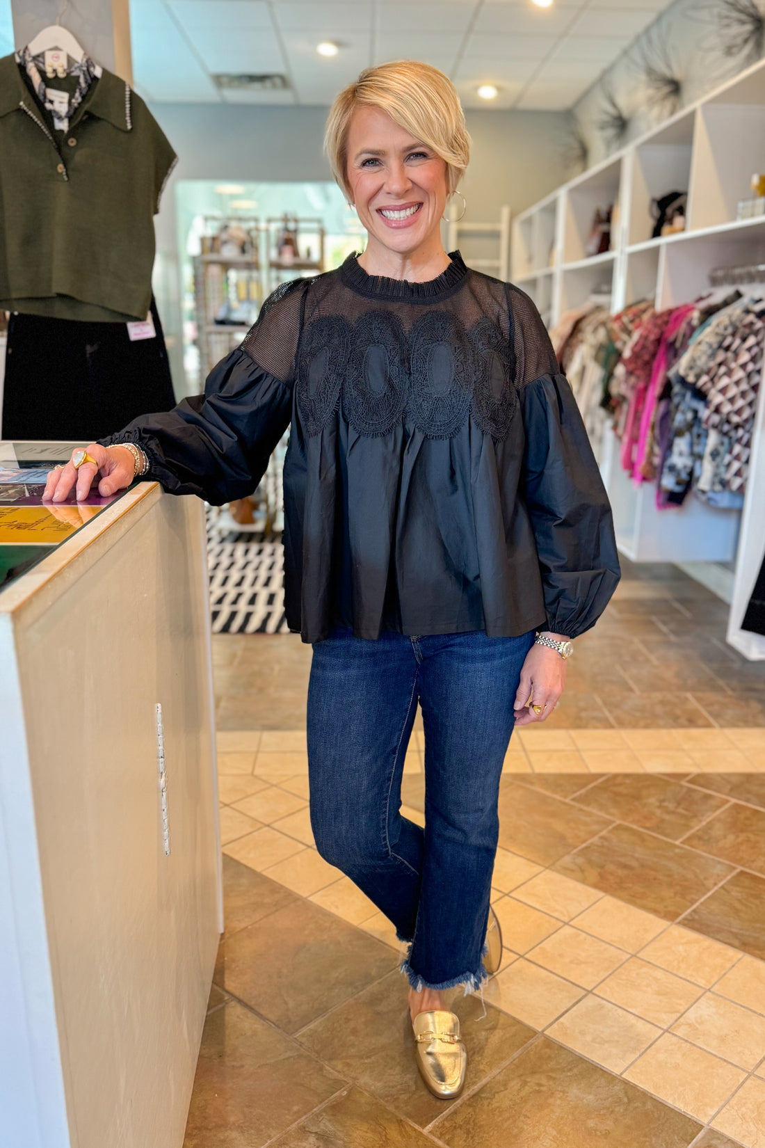 Woman in a black top and blue jeans standing in a store.