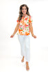 Front view of woman wearing Orange & Multi Floral Peplum Top by Fate with white jeans against white studio background.