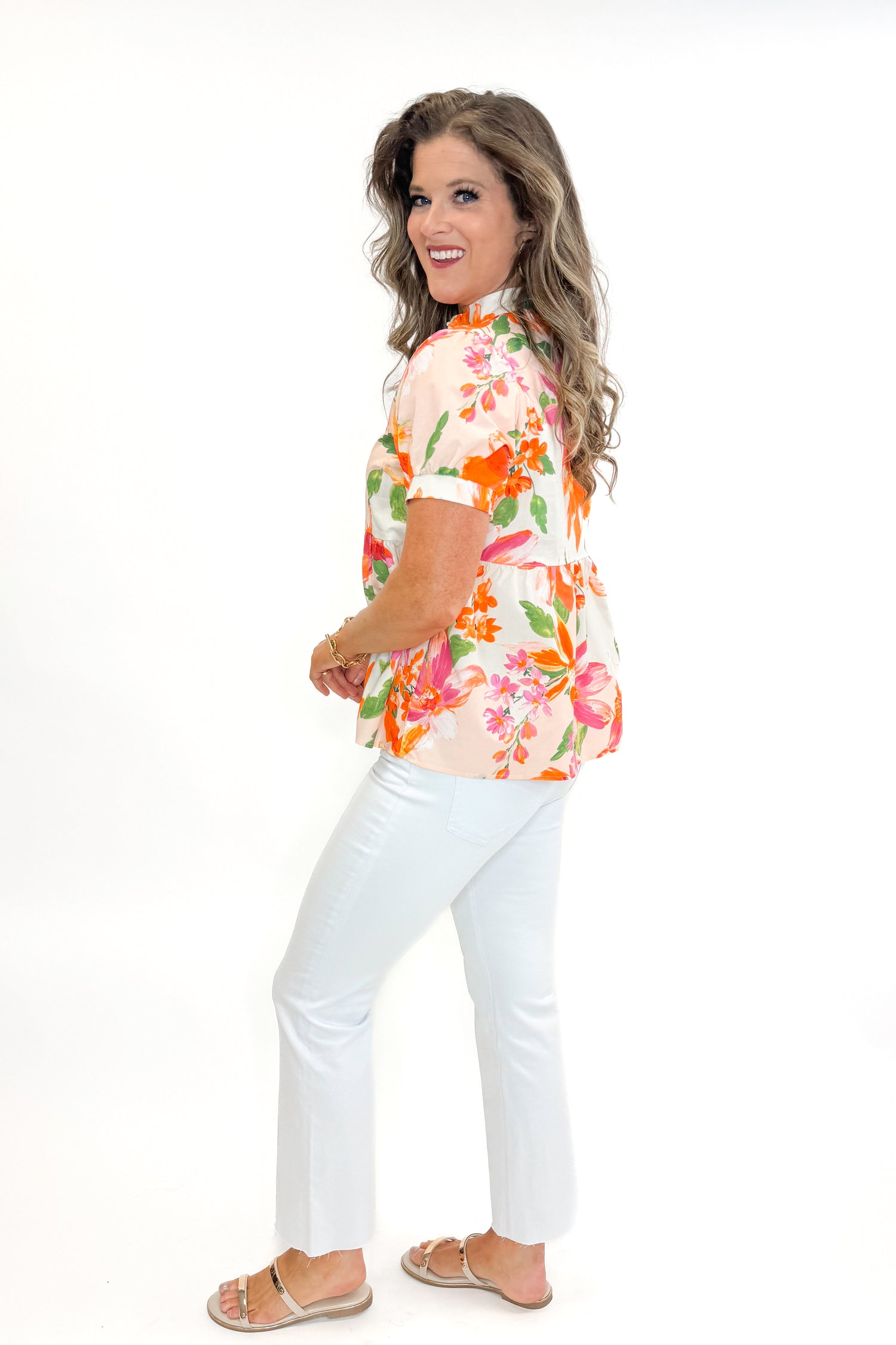 Side view of woman wearing Orange &amp; Multi Floral Peplum Top by Fate with white jeans against white studio background.