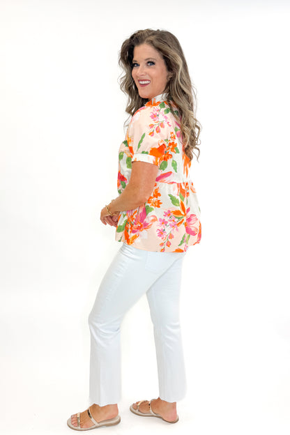 Side view of woman wearing Orange &amp; Multi Floral Peplum Top by Fate with white jeans against white studio background.