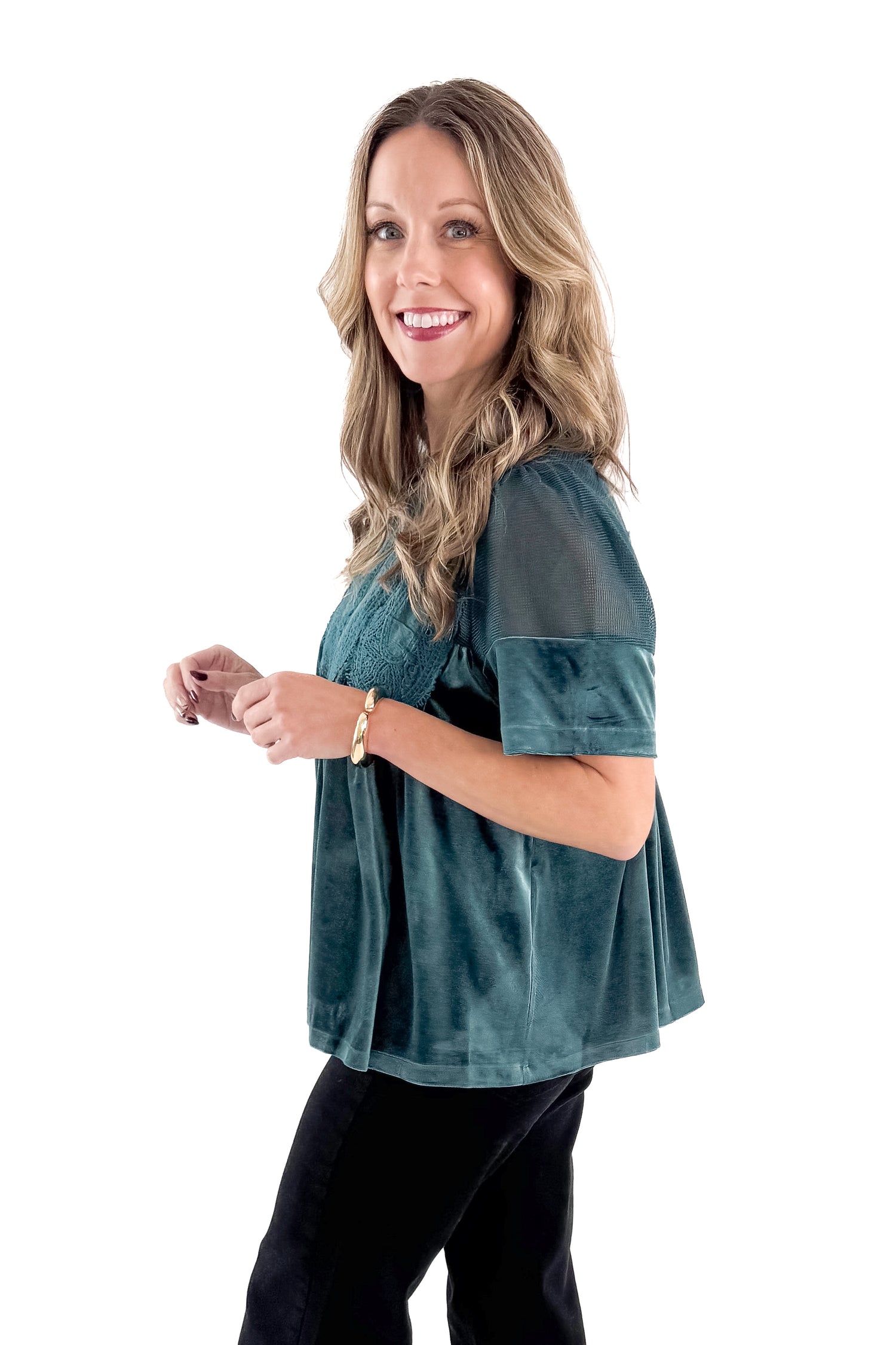Side view of woman wearing Teal Velvet With Lace Applique Top with jeans against white studio background.