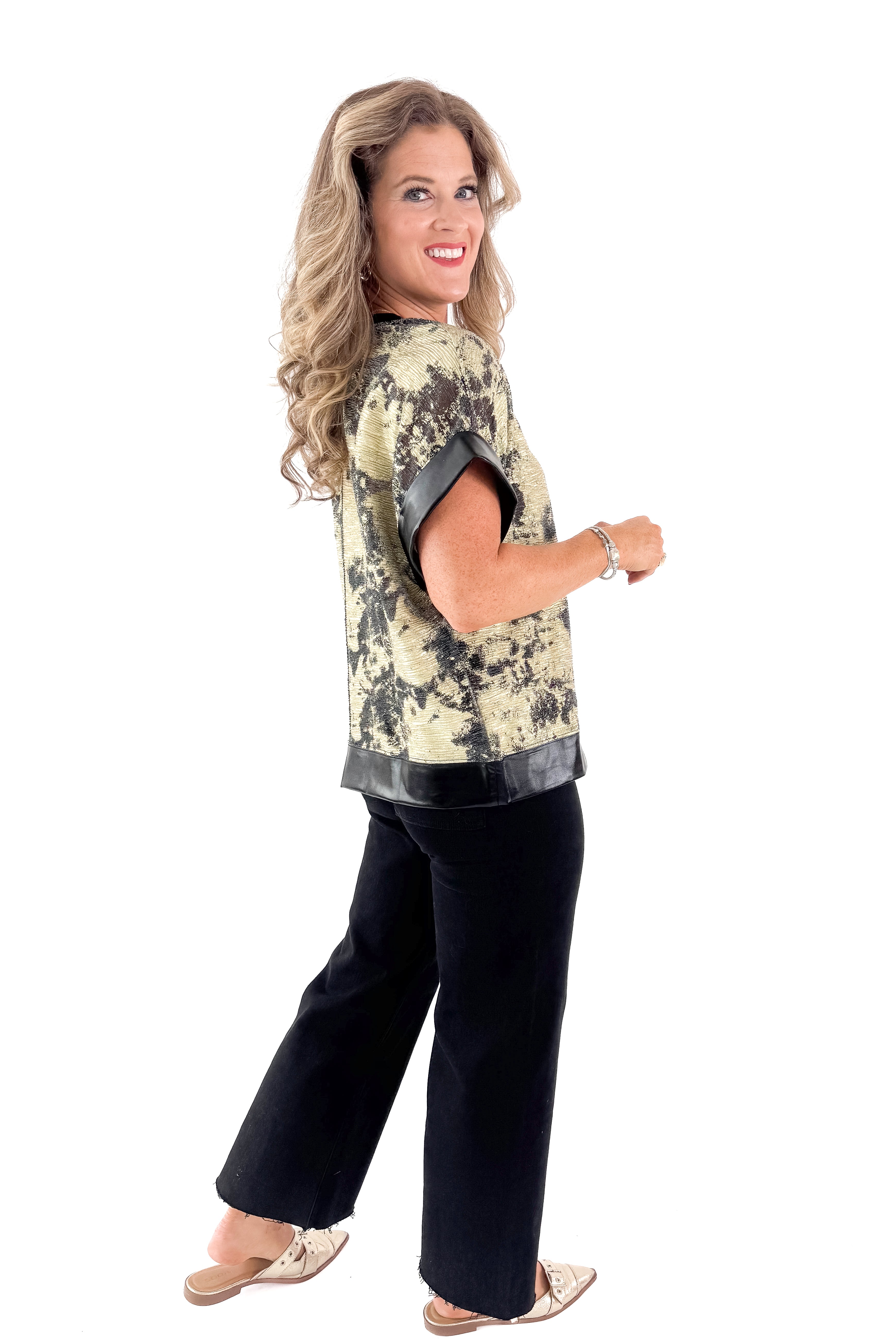 Side view of woman wearing Black &amp; Gold Metallic Abstract Print Top with jeans against white studio background.