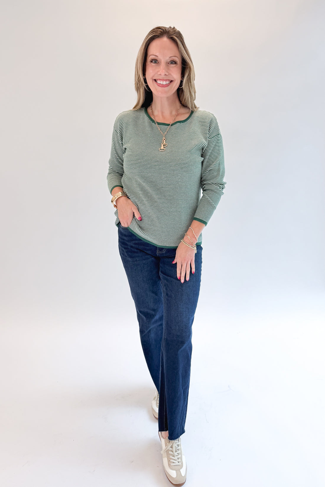 Front view of woman wearing Swagger Boutique’s Forest Green Striped Sweater with jeans against white studio background.