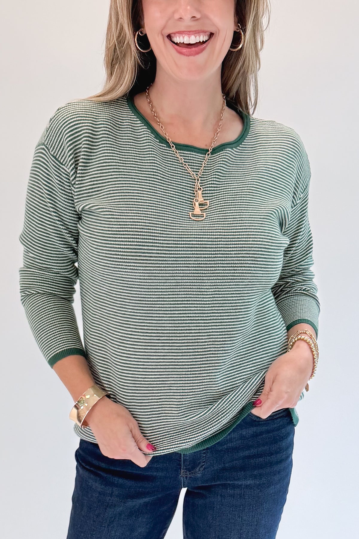 Front detail view of woman wearing Swagger Boutique’s Forest Green Striped Sweater with jeans against white studio background.