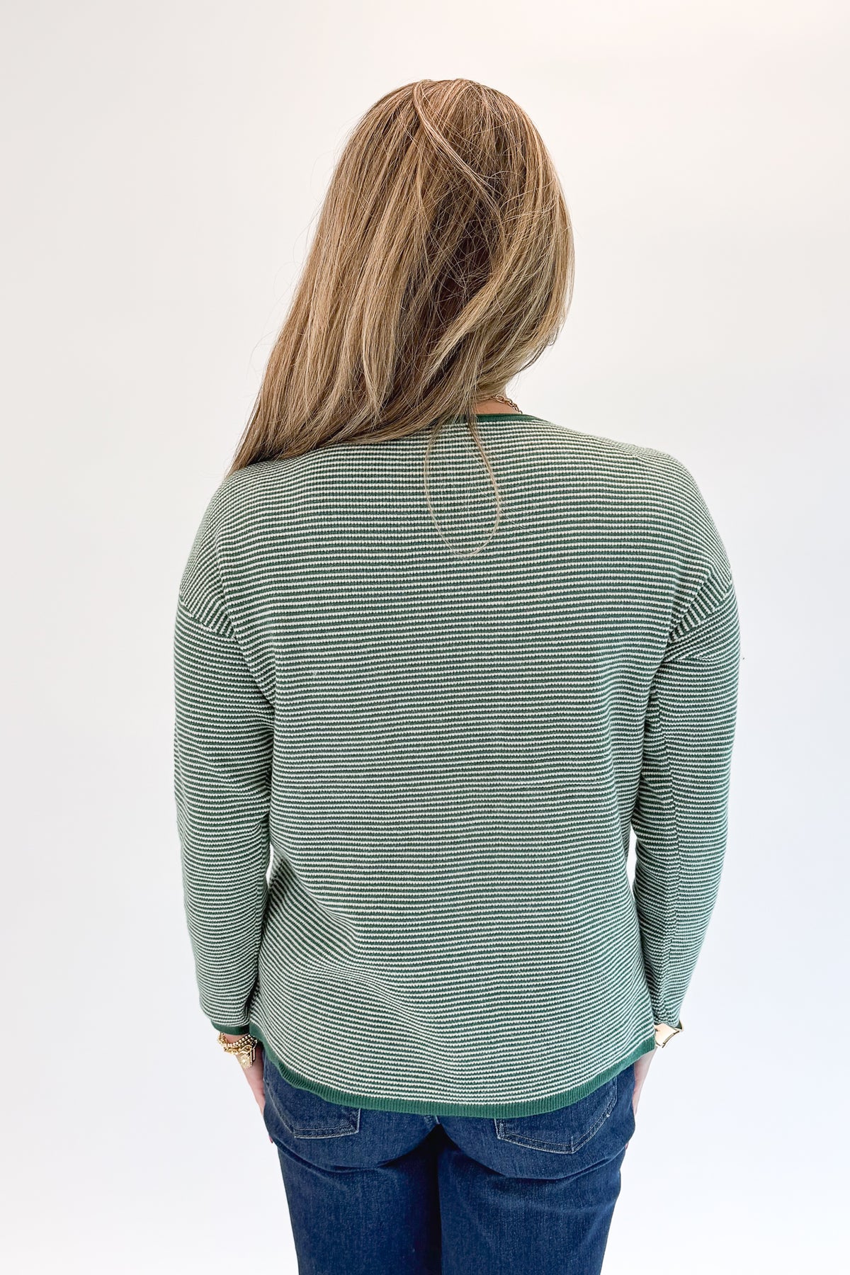 Back view of woman wearing Swagger Boutique’s Forest Green Striped Sweater with jeans against white studio background.
