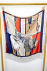 A square silk scarf with fringe, featuring a vintage-style illustration a horse, draped over a gold-colored clothing rack against a white wall.