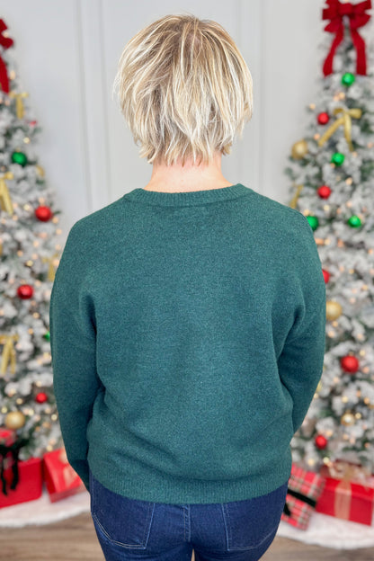 Person wearing a teal sweater in front of Christmas trees with decorations.