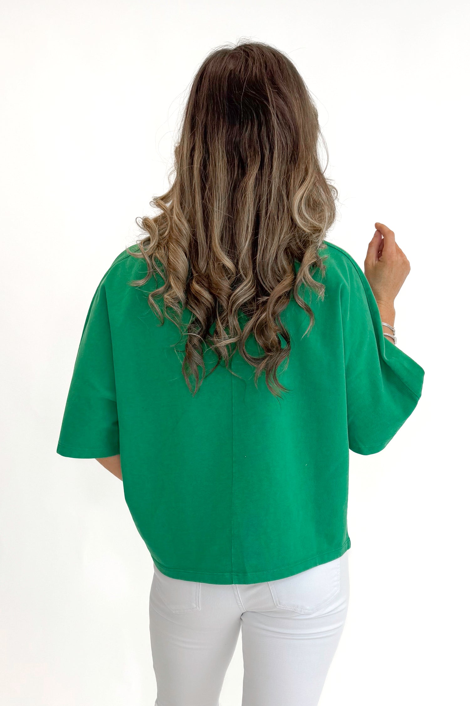 Back view of woman wearing Green Washed Boxy Tee with jeans against white studio background.