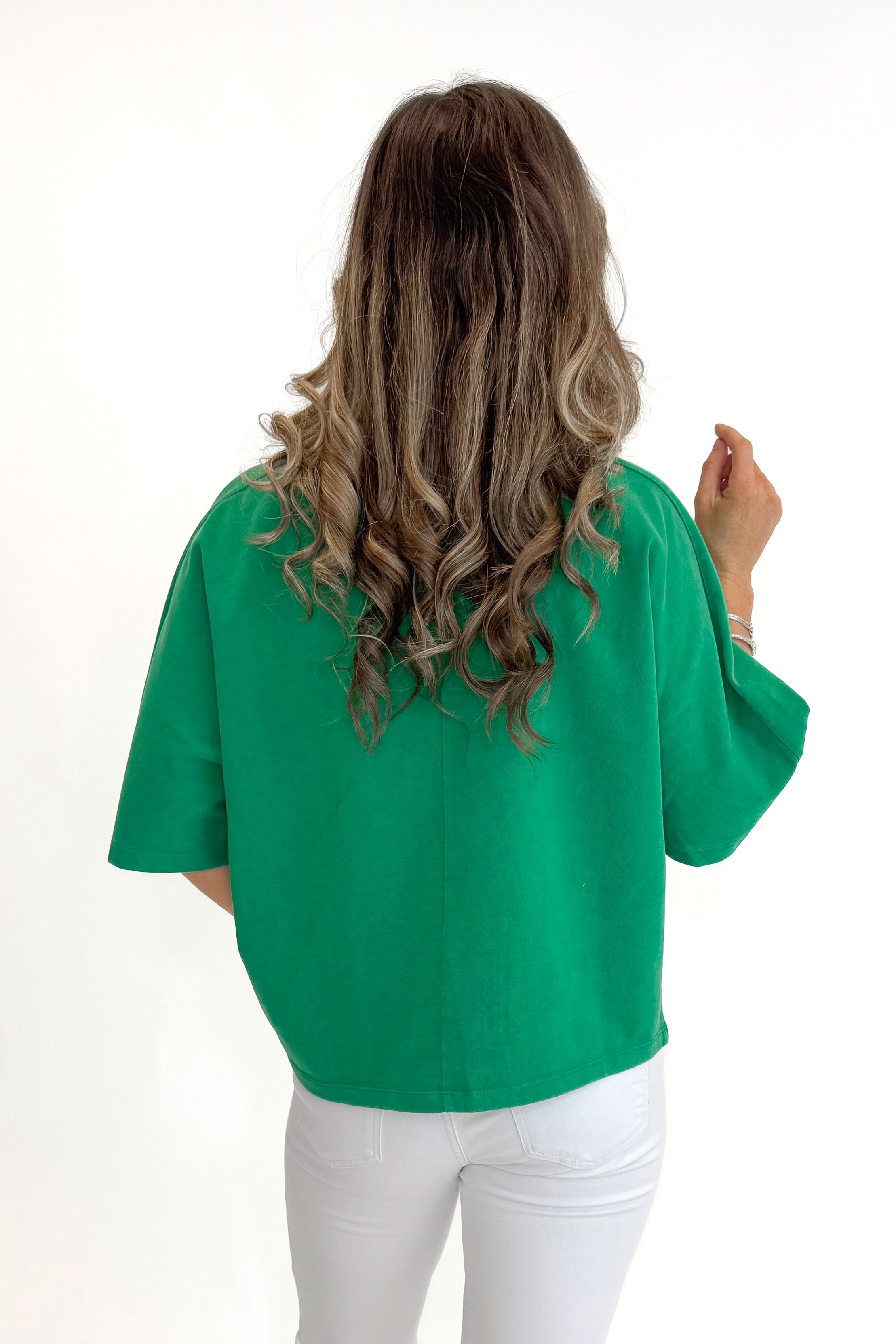 Back view of woman wearing Green Washed Boxy Tee with jeans against white studio background.