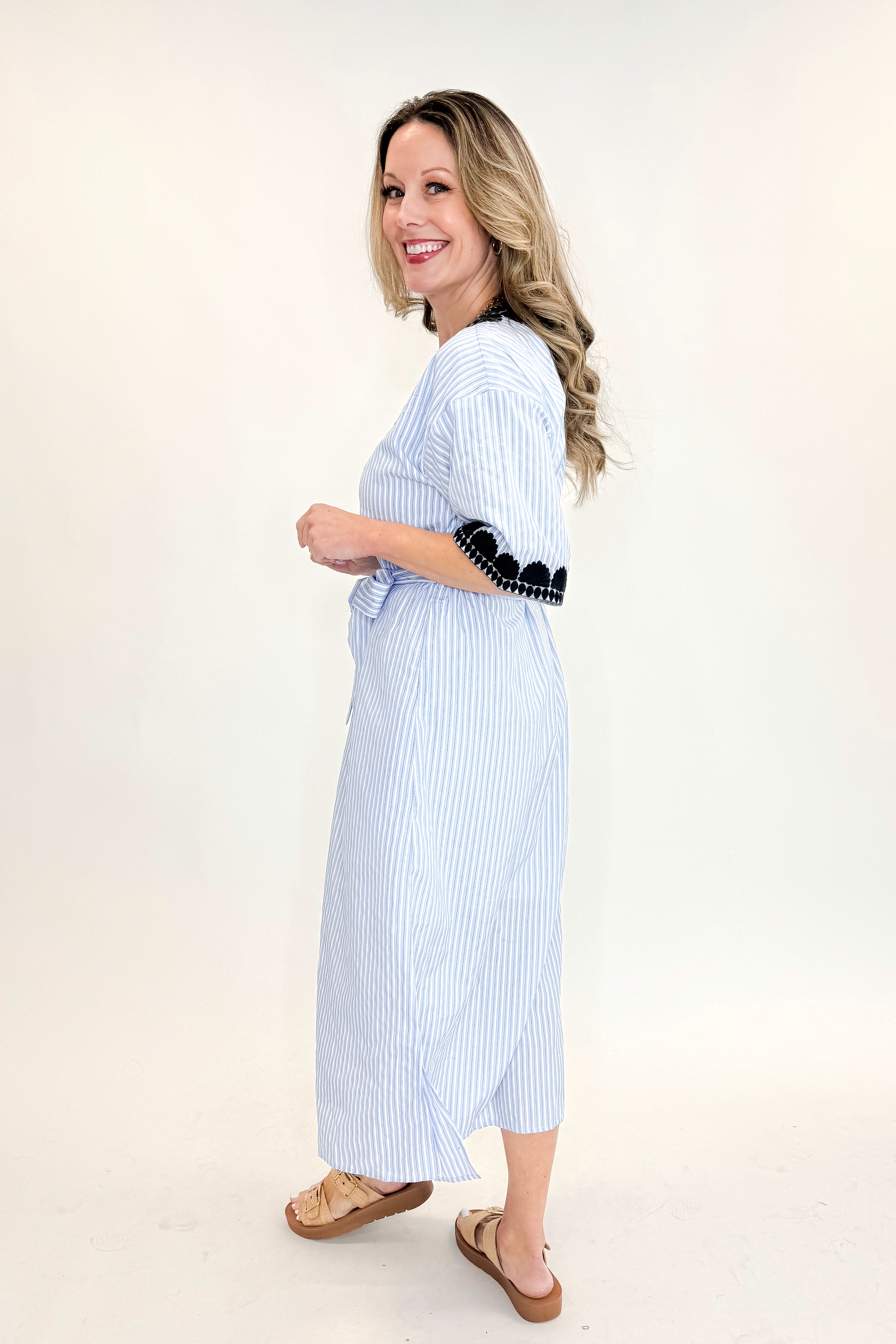 Side view of woman wearing Blue Striped Embroidery Accent Midi Dress with sandals against white studio background.