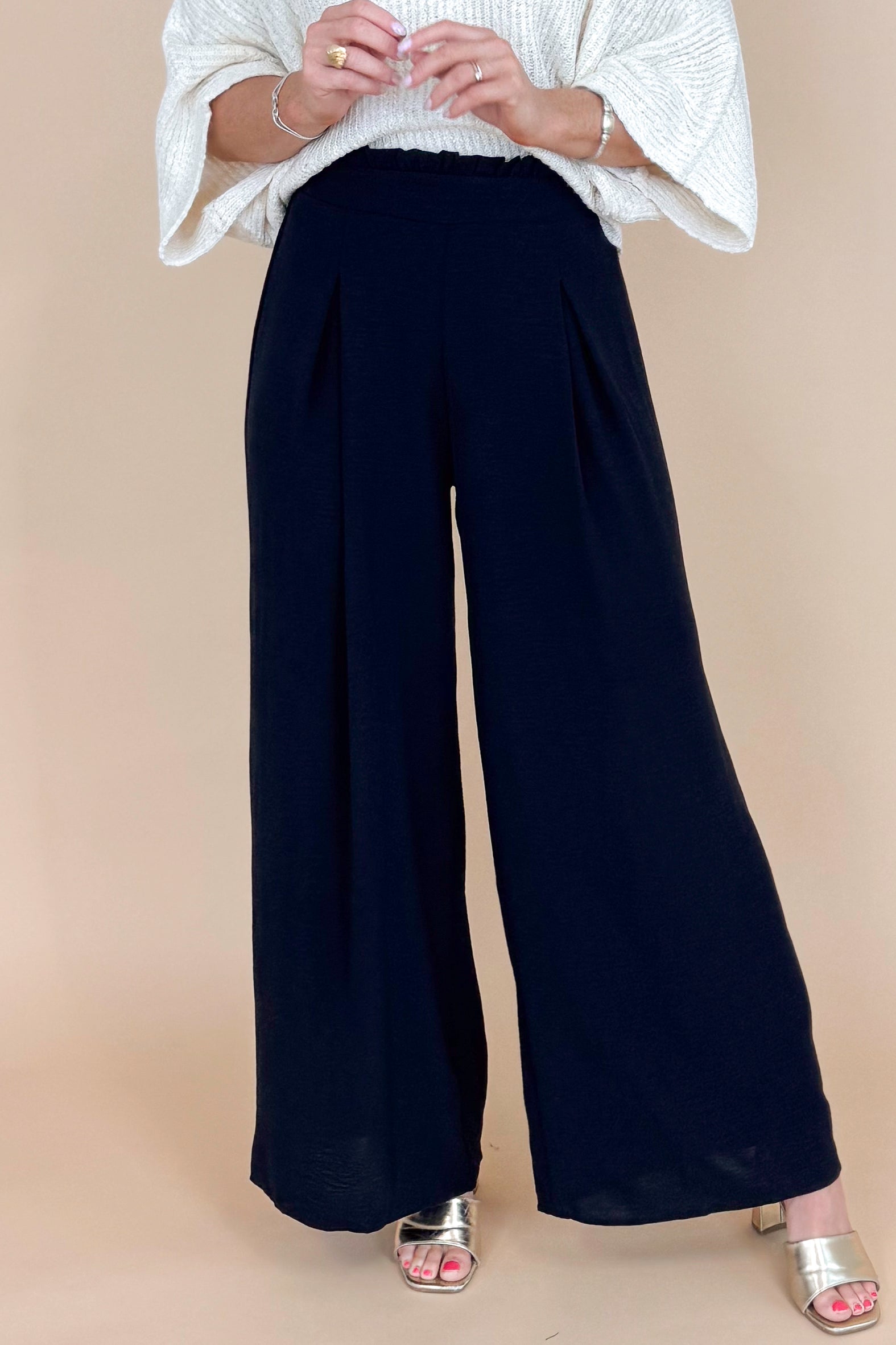 Person wearing a white top and black wide-leg pants on a beige background