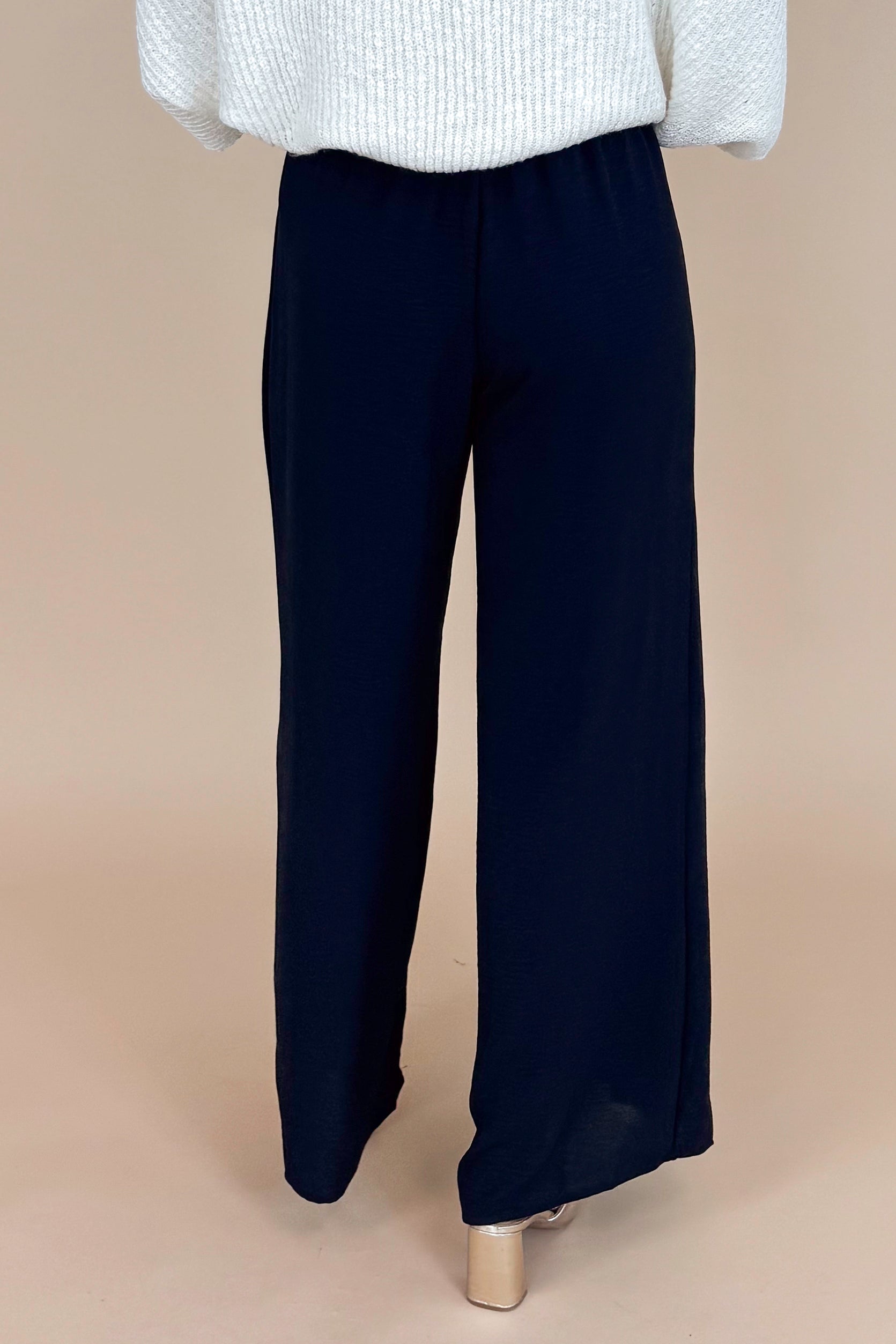 Black wide-leg pants worn with a light gray sweater on a beige background