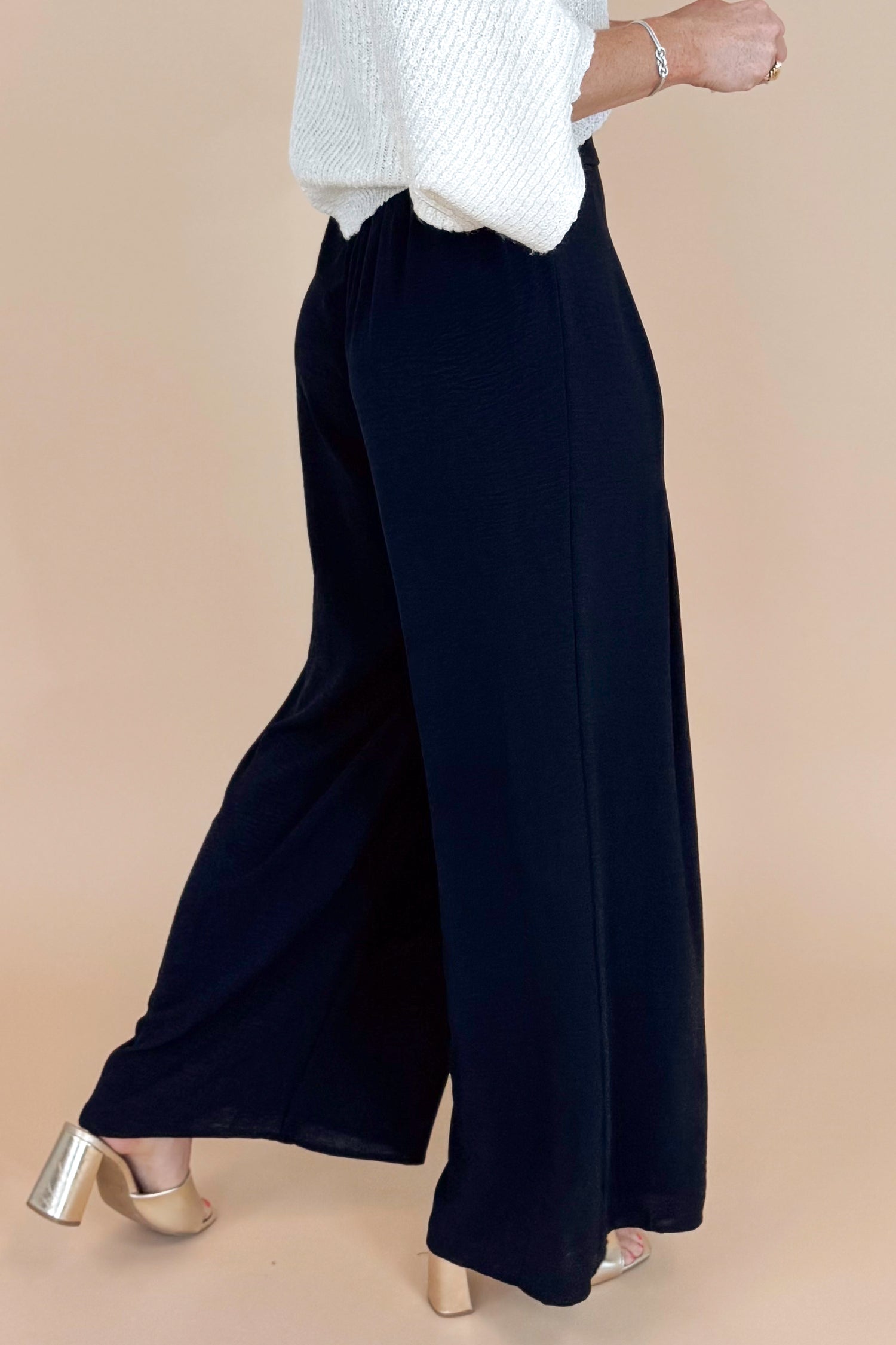 Person wearing black wide-leg pants and a white top on a beige background