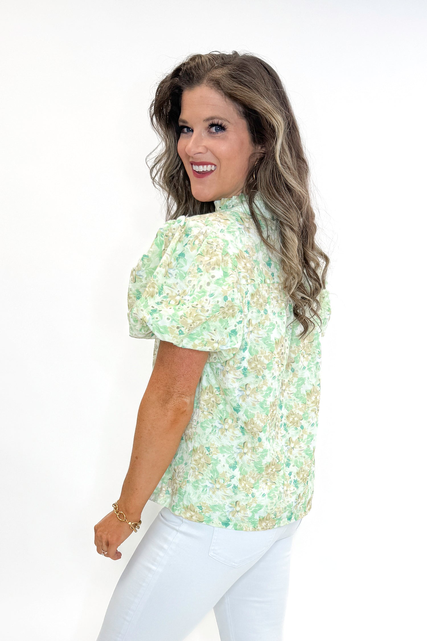 Side view of woman wearing Green &amp; Yellow Floral Eyelet Top with white jeans against white studio background.