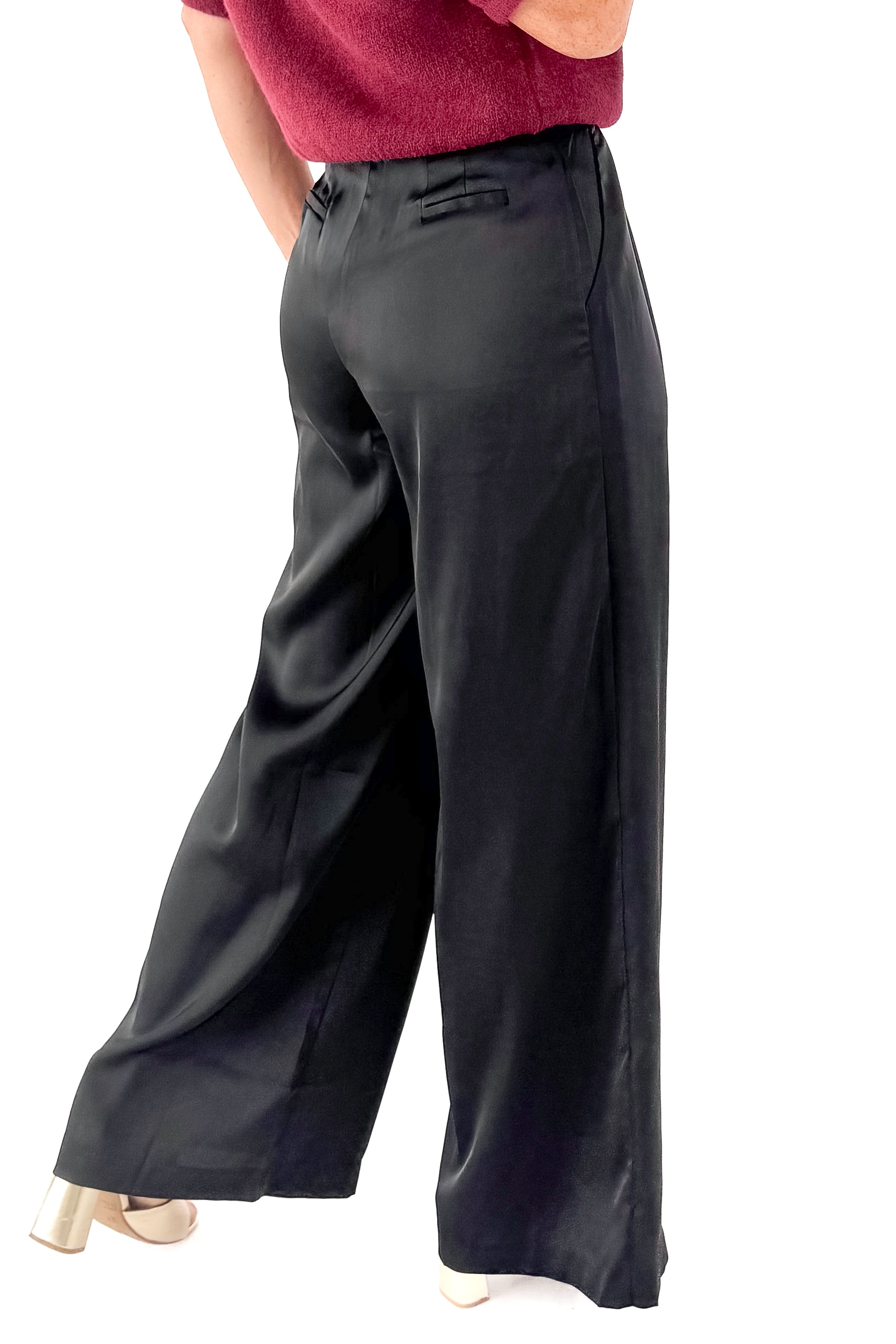 Side view of woman wearing sweater with black satin pleated pants against white studio background.