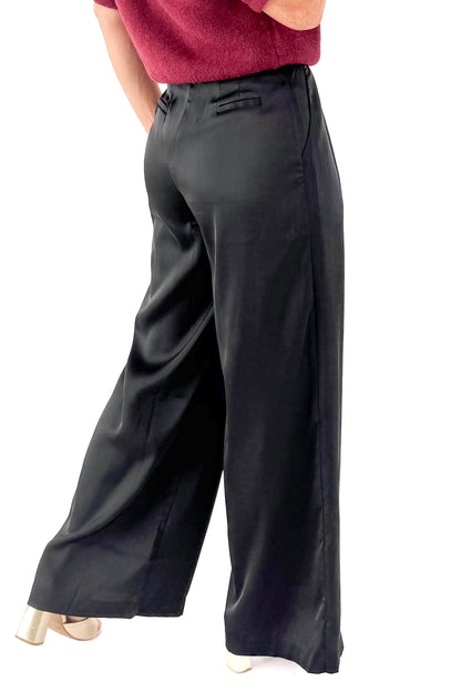 Side view of woman wearing sweater with black satin pleated pants against white studio background.