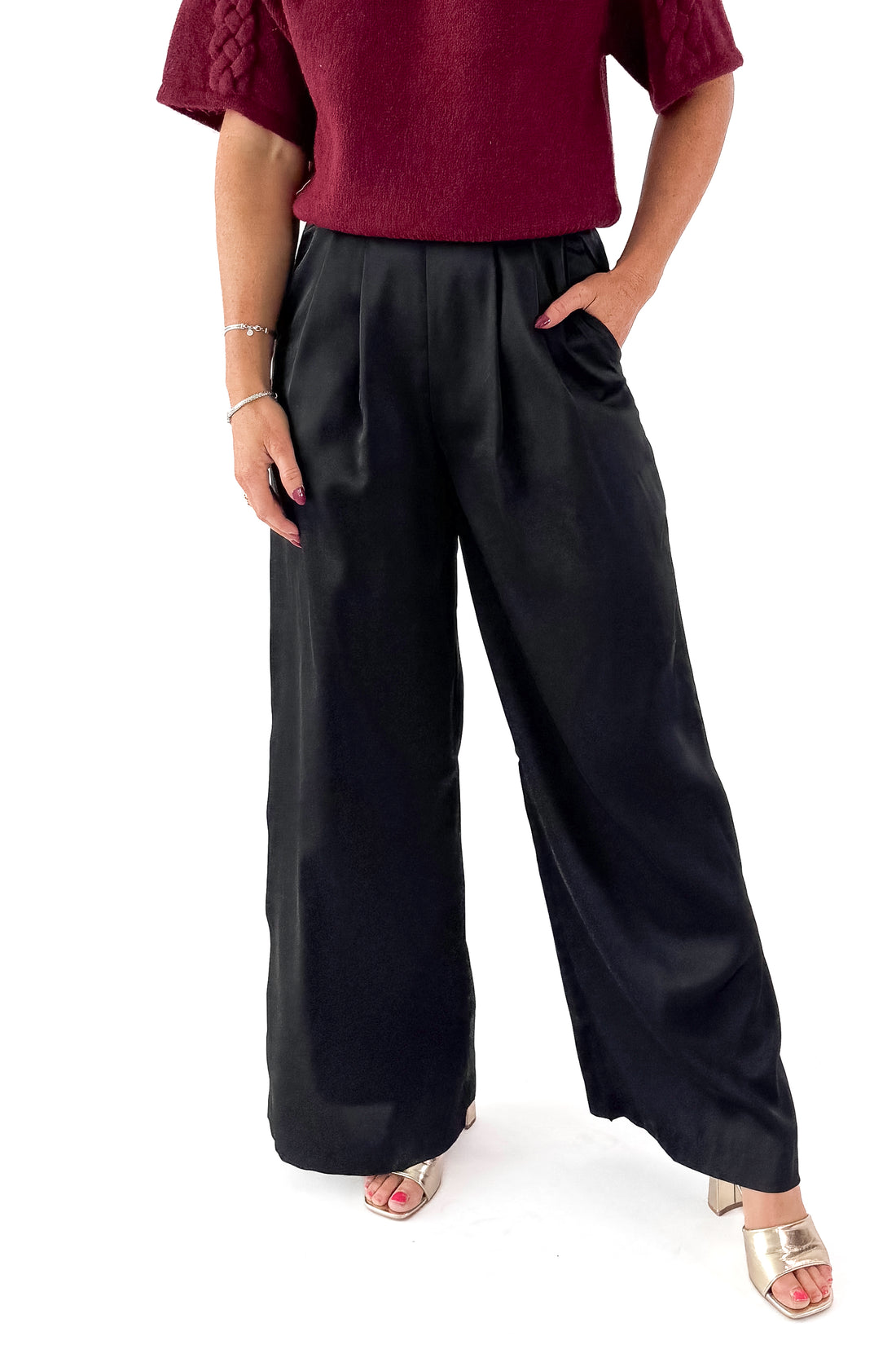 Front view of woman wearing sweater with black satin pleated pants against white studio background.
