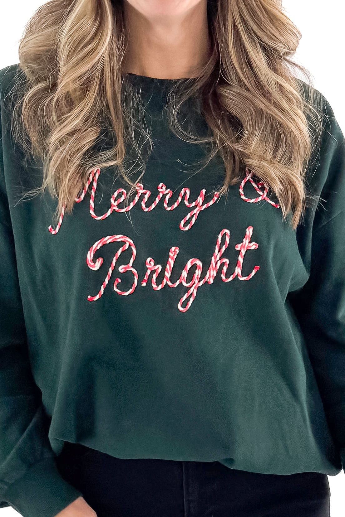 Front detail view of woman wearing Garland Green Bright Sunday Sweatshirt with jeans against white studio background.
