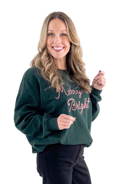 Side view of woman wearing Garland Green Bright Sunday Sweatshirt with jeans against white studio background.