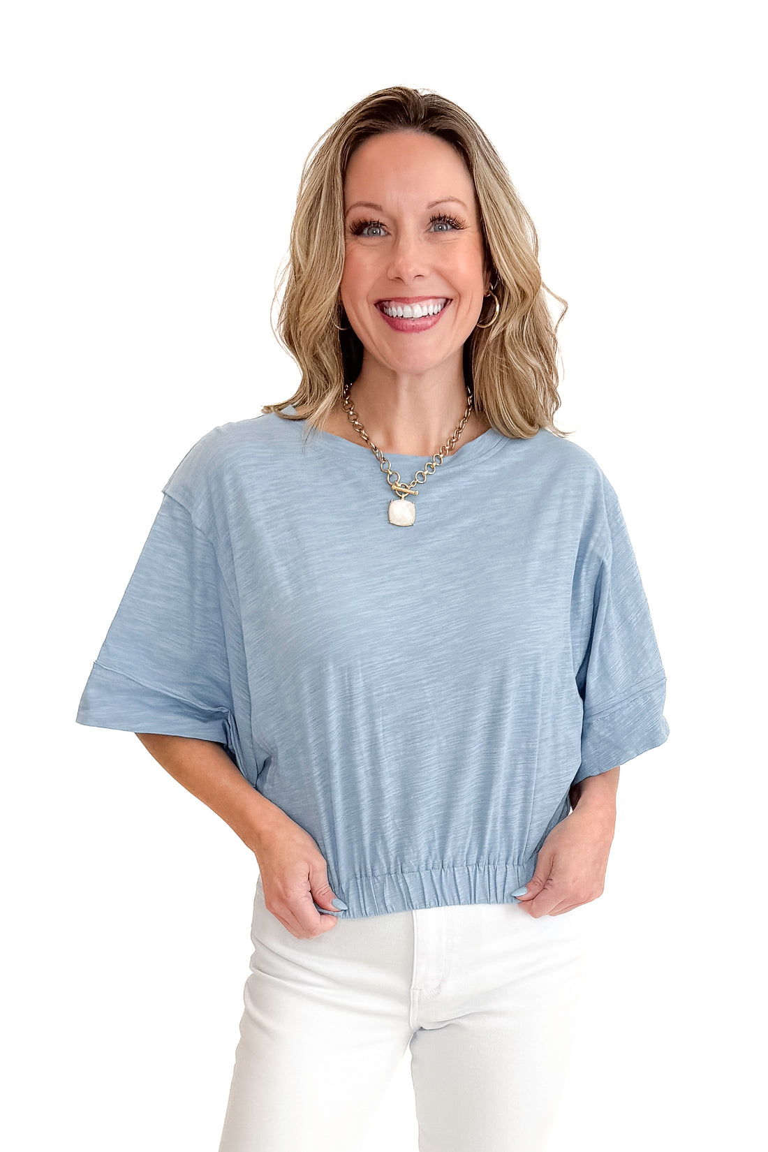 Front view of woman wearing Blue Cinched Bottom Tee with jeans against white studio background.