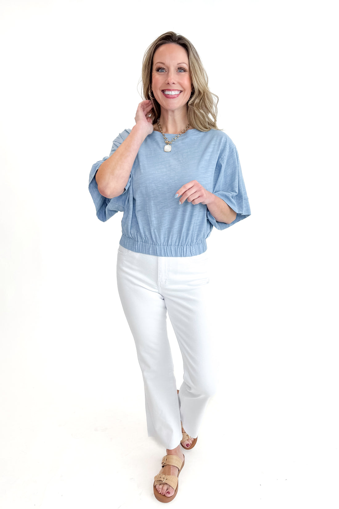 Front view of woman wearing Blue Cinched Bottom Tee with jeans against white studio background.