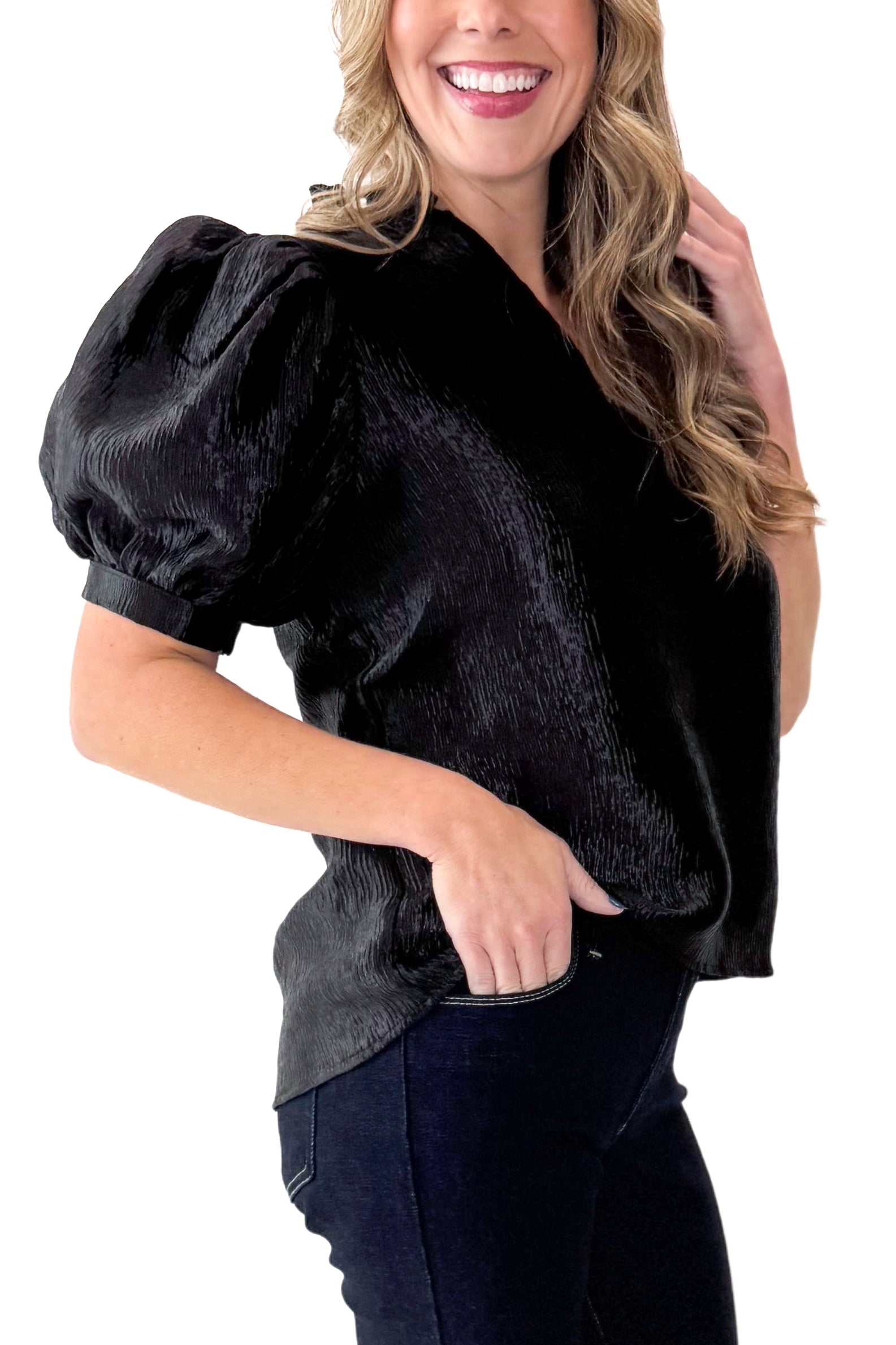 Side view of woman wearing Black Sheen Textured Puff Sleeve Top with jeans against white studio background.