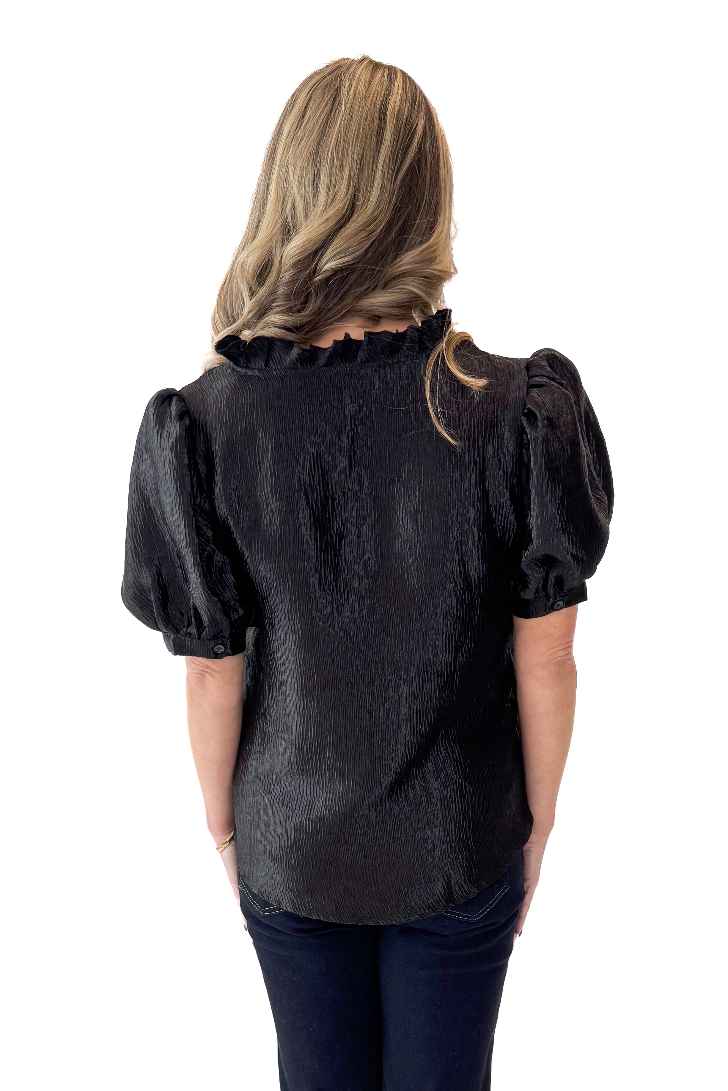 Back view of woman wearing Black Sheen Textured Puff Sleeve Top with jeans against white studio background.