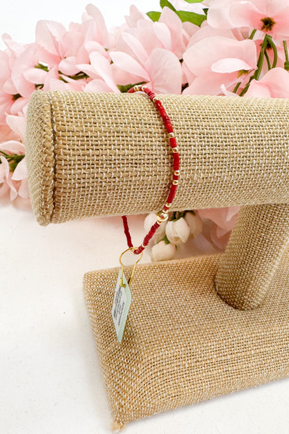 Red bracelet on a burlap roll with pink flowers in the background