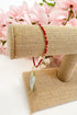 Red bracelet on a burlap roll with pink flowers in the background