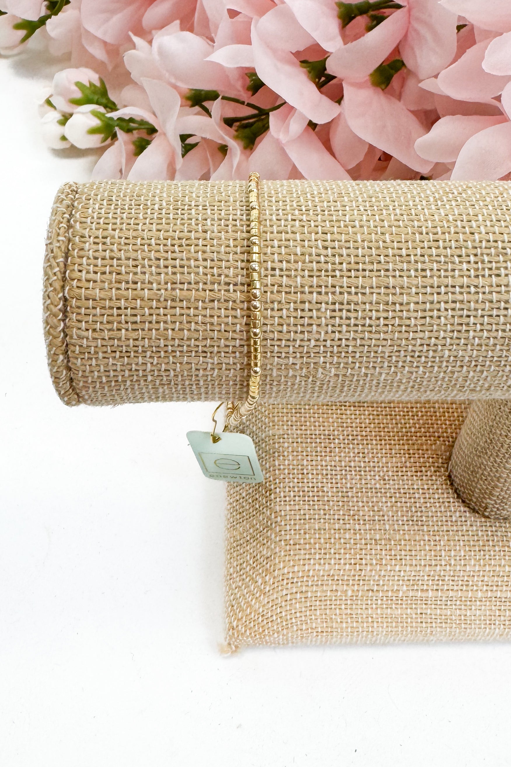 gold bracelet on beige burlap fabric with a tag on a white background