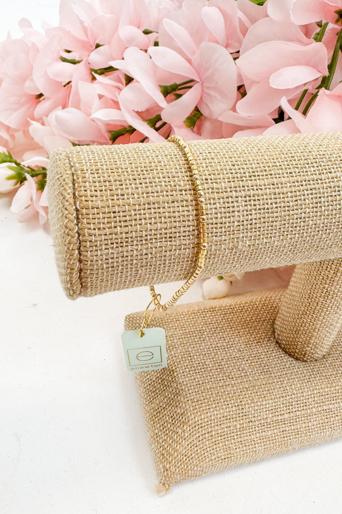 Gold bracelet on a beige fabric with pink flowers in the background