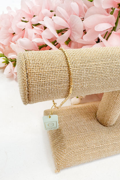 Gold bracelet on a beige fabric with pink flowers in the background