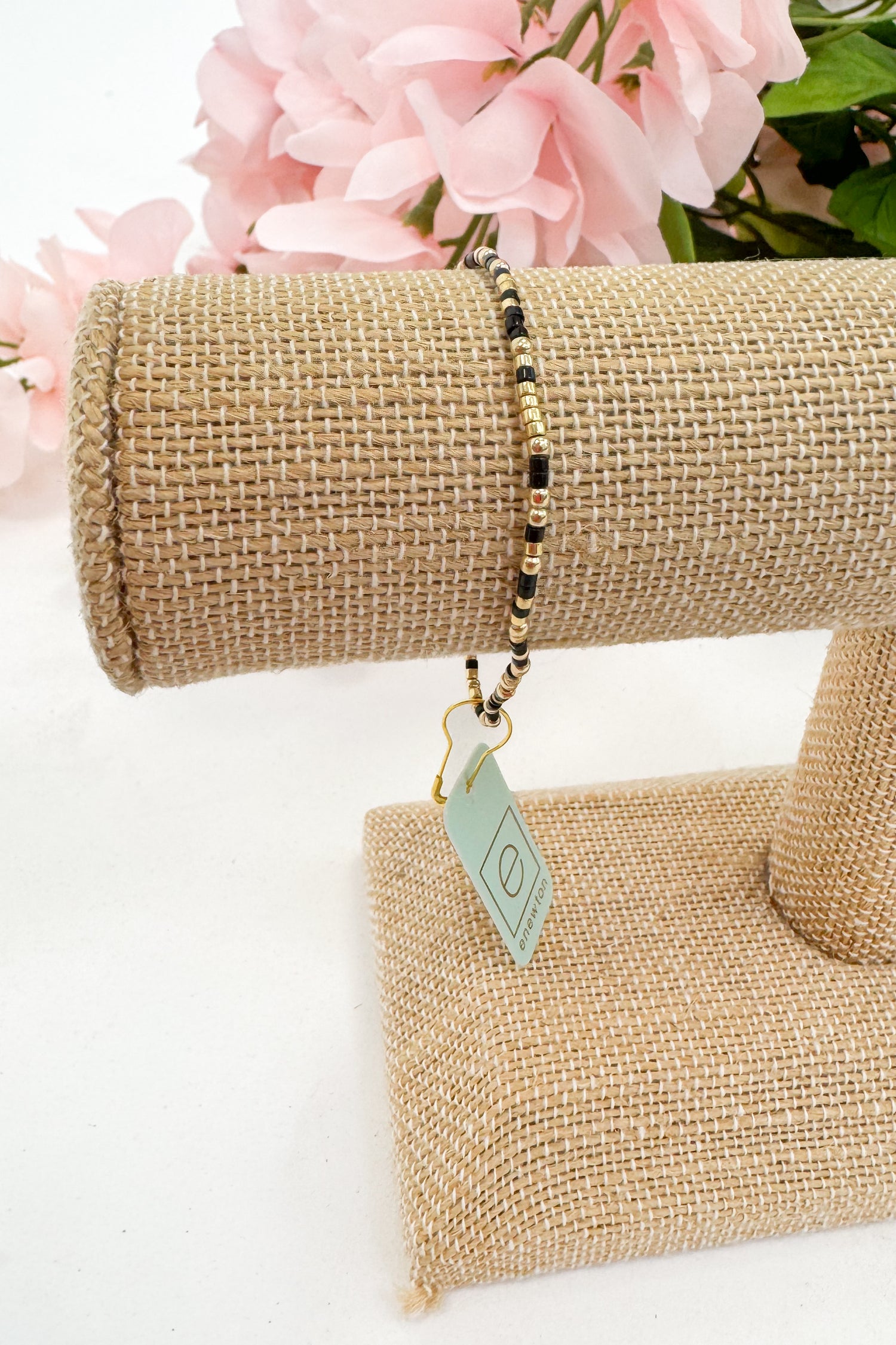 Bracelet on a burlap stand with pink flowers in the background
